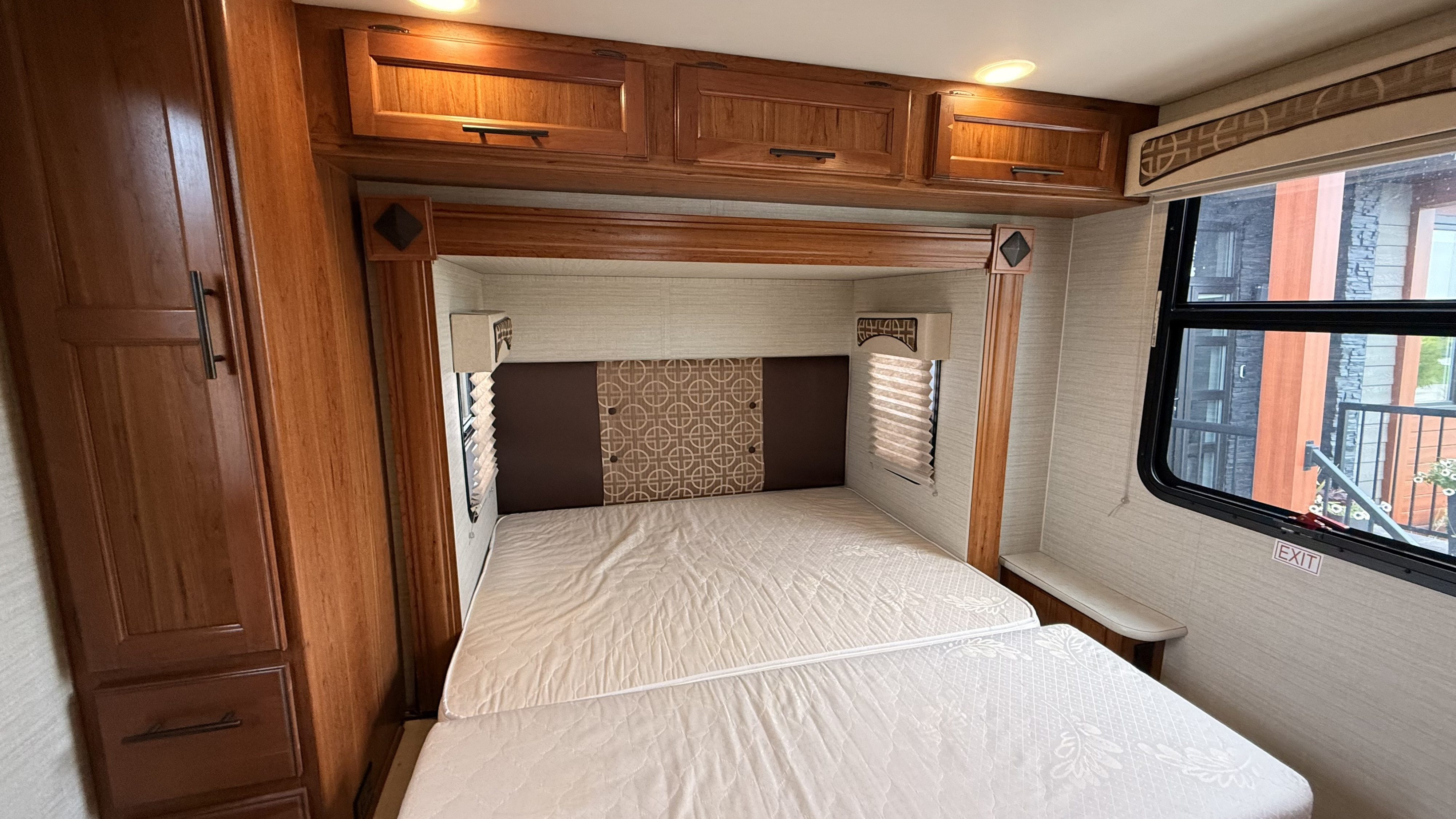 This cozy rv rental features a fold-down bed, rich wooden cabinetry, and a window with an 'EXIT' sign for safety.. Jayco Melbourne 2017
