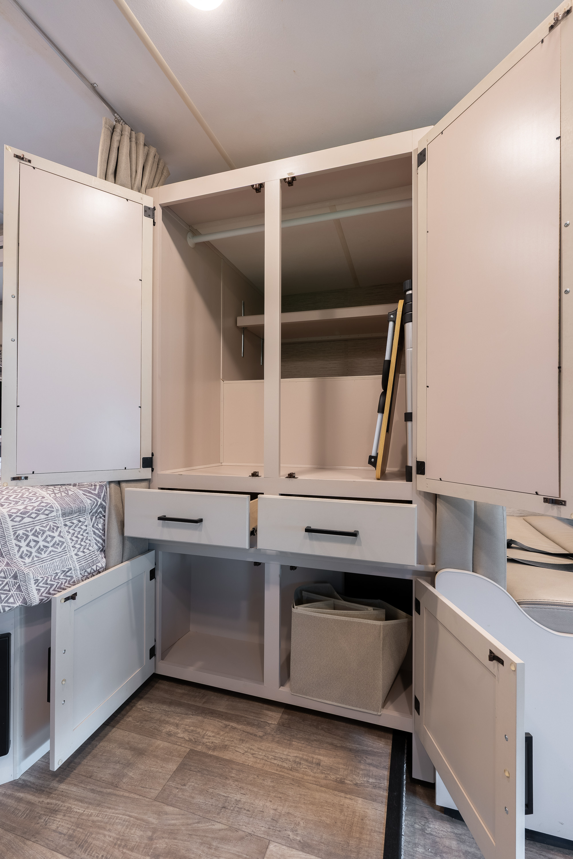 Organized RV rental storage: open wardrobe with hanging rods, drawers, and bins next to a sleeping area.. Thor Chateau 2023