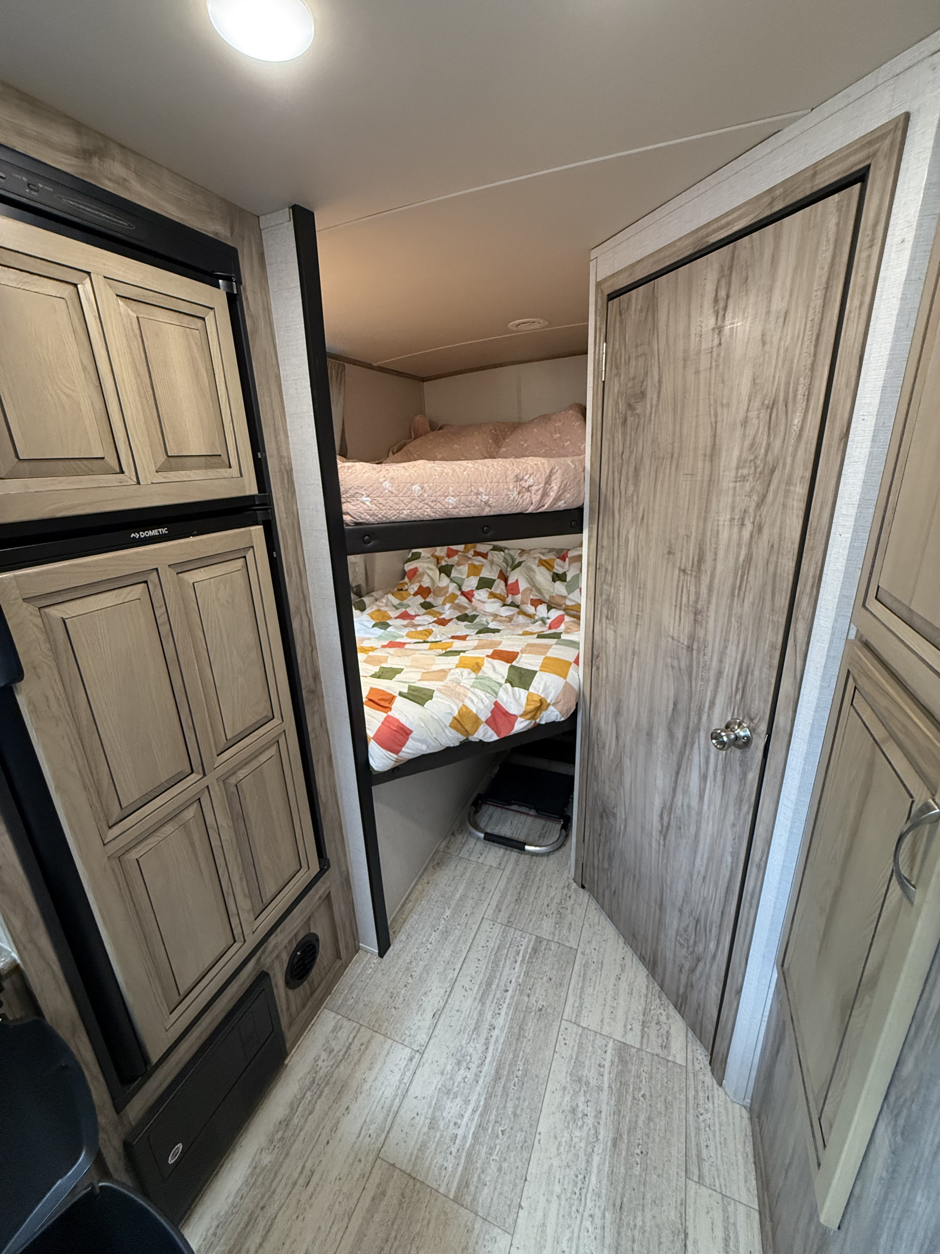 Interior of an RV rental featuring bunk beds with patterned quilts, a Dometic fridge, and wood-look flooring.. Palomino Solaire 240BHS 2018
