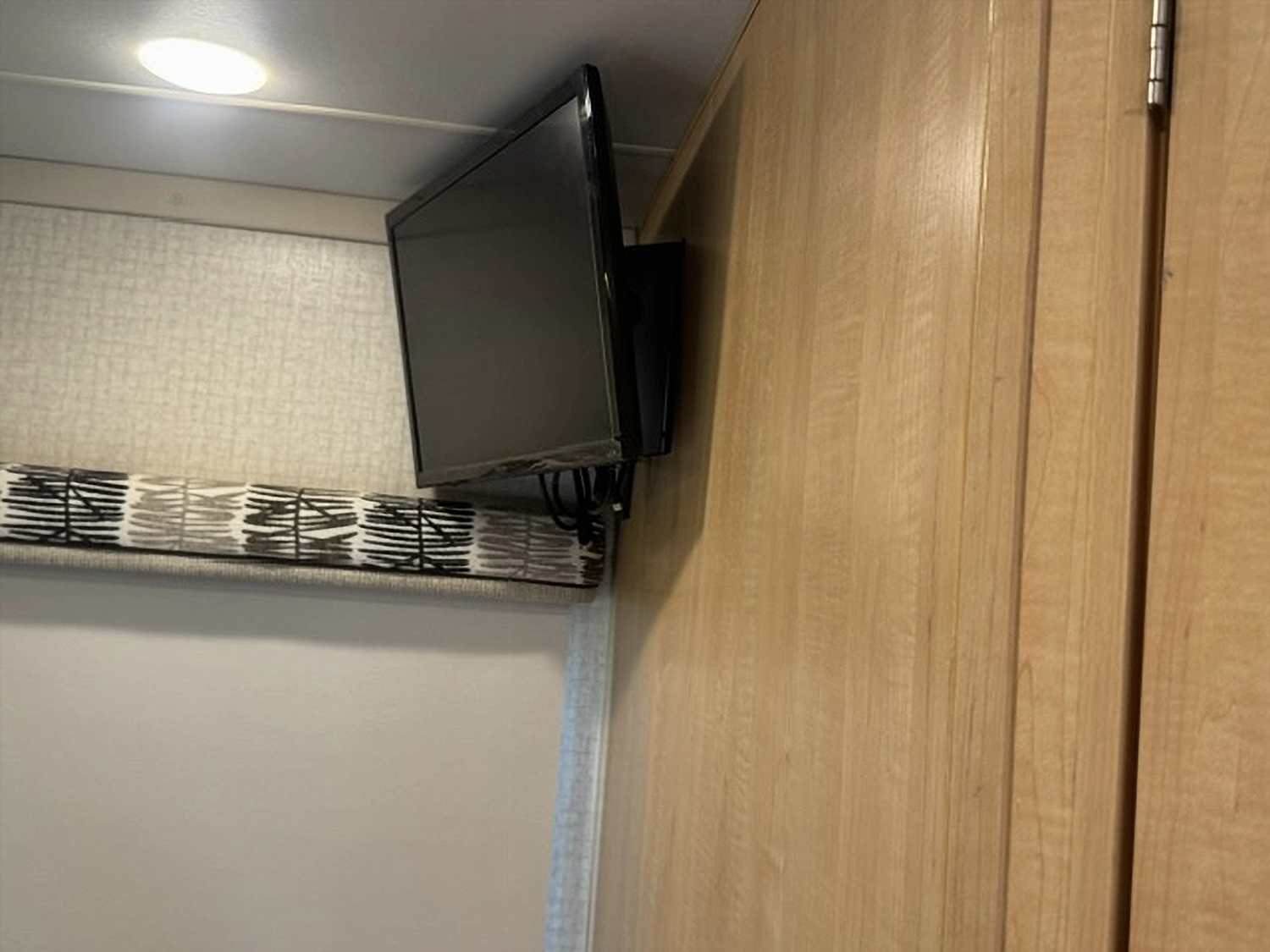 RV rental interior: Wall-mounted TV above a patterned shade, with light wood cabinetry and a ceiling light fixture.. Winnebago Fuse 2017