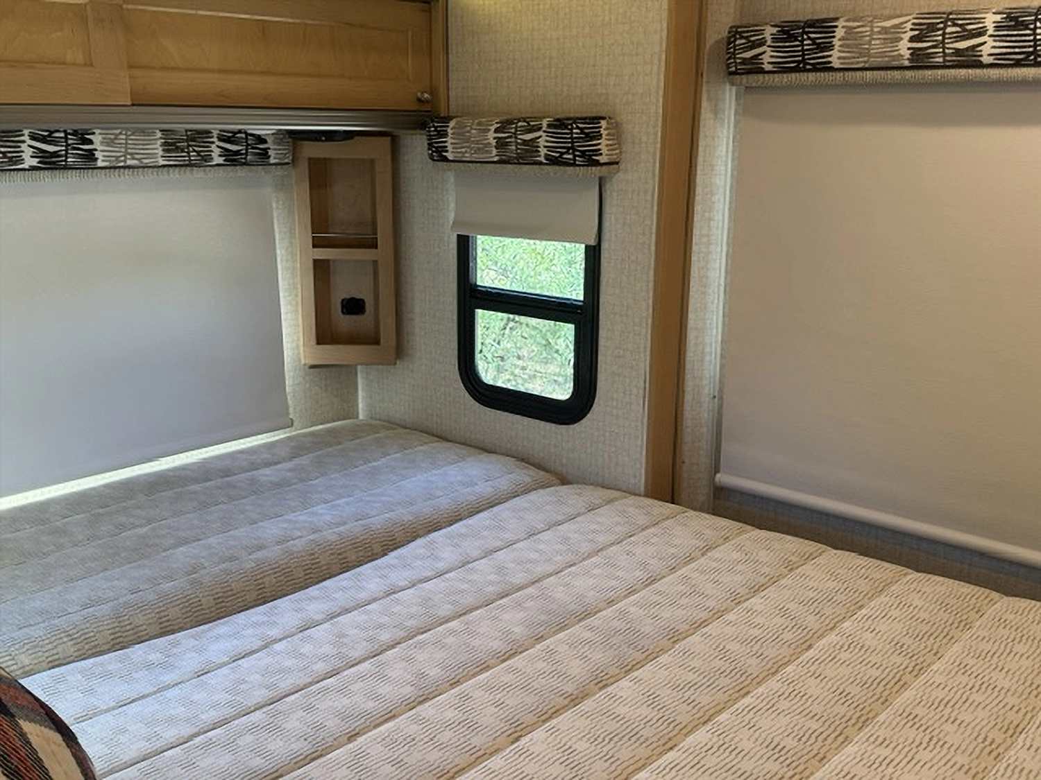 This RV rental features a cozy bedroom with two neatly made twin beds, windows with blinds, and a small wooden shelf.. Winnebago Fuse 2017
