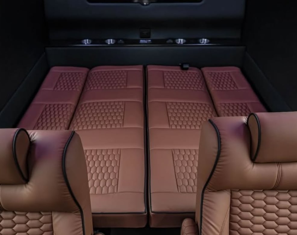 RV rental interior showing comfortable brown seats folded into a sleeping area with unique quilted patterns.. Mercedes Benz Executive Lounger by Legends Sprinter 3500xd 170 Ext AWD Executive Lounger 2023