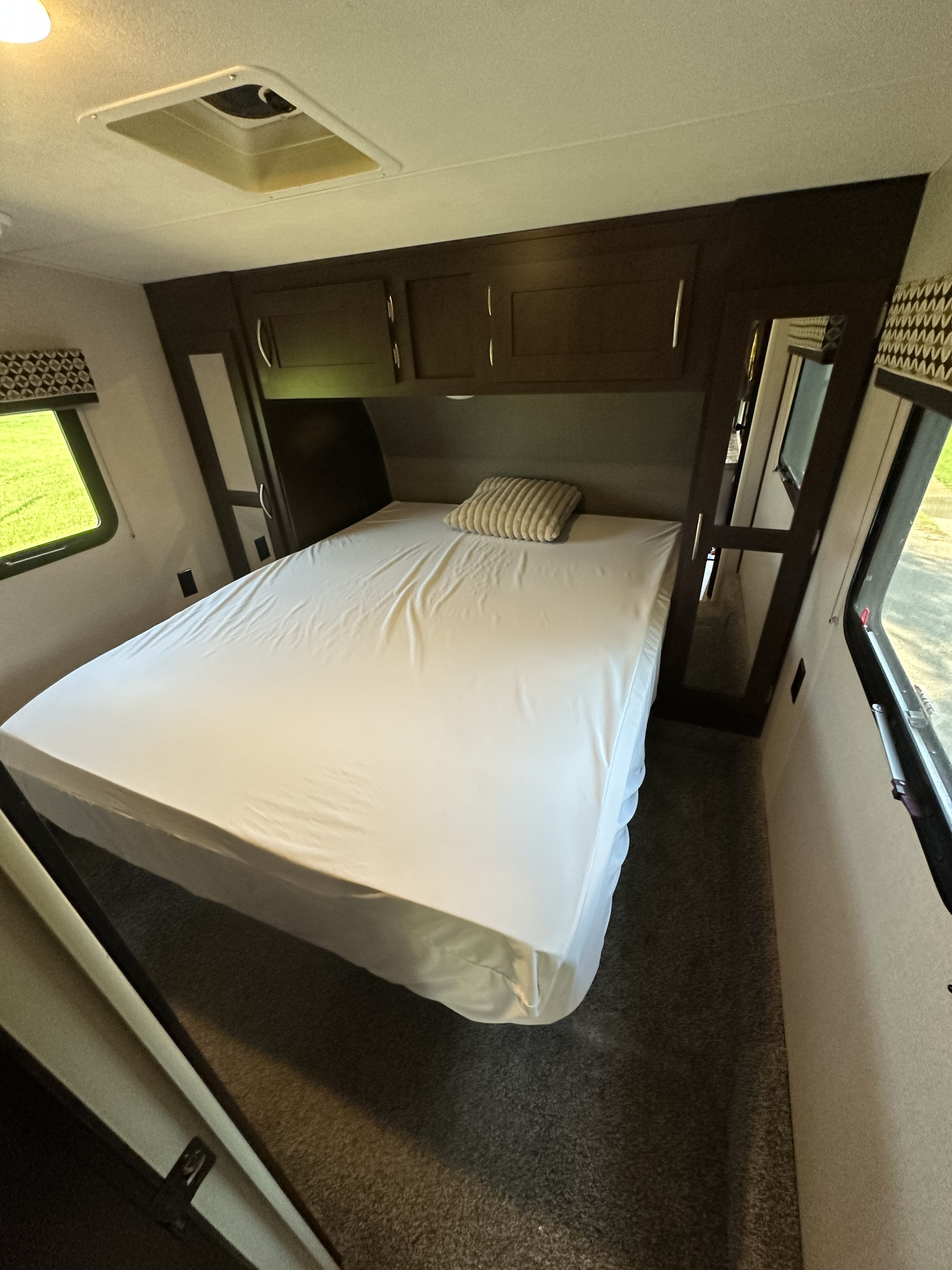 Inside a cozy RV rental bedroom. A neatly made bed is flanked by windows, with overhead storage visible above.. Sportsmen Sportsmen Fifth Wheel 2018