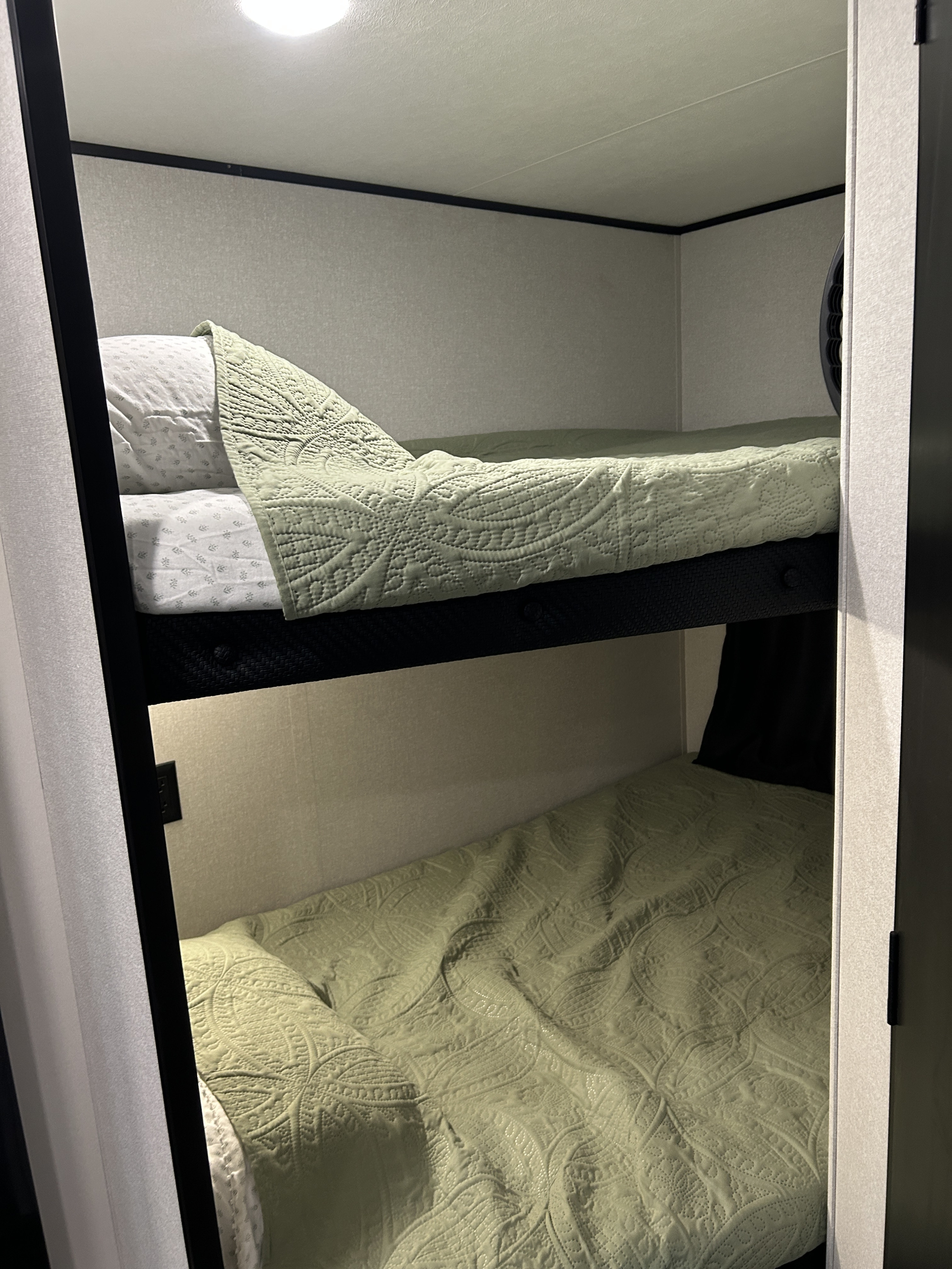 Cozy bunk beds in an RV rental, featuring light green quilted blankets and pillows for compact travel sleeping.. Jayco Jay Flight SLX 2026