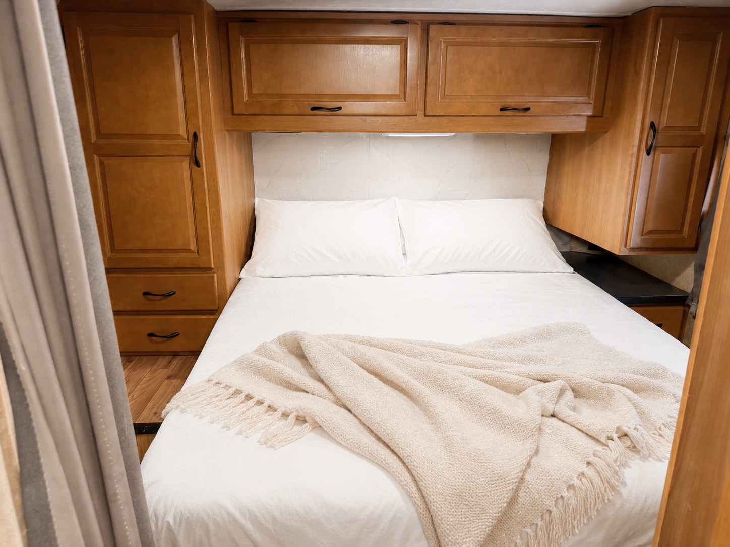 Cozy RV rental bedroom with comfortable white bed, wood cabinetry, and a soft throw blanket for a relaxing journey.. Thor Majestic 2017