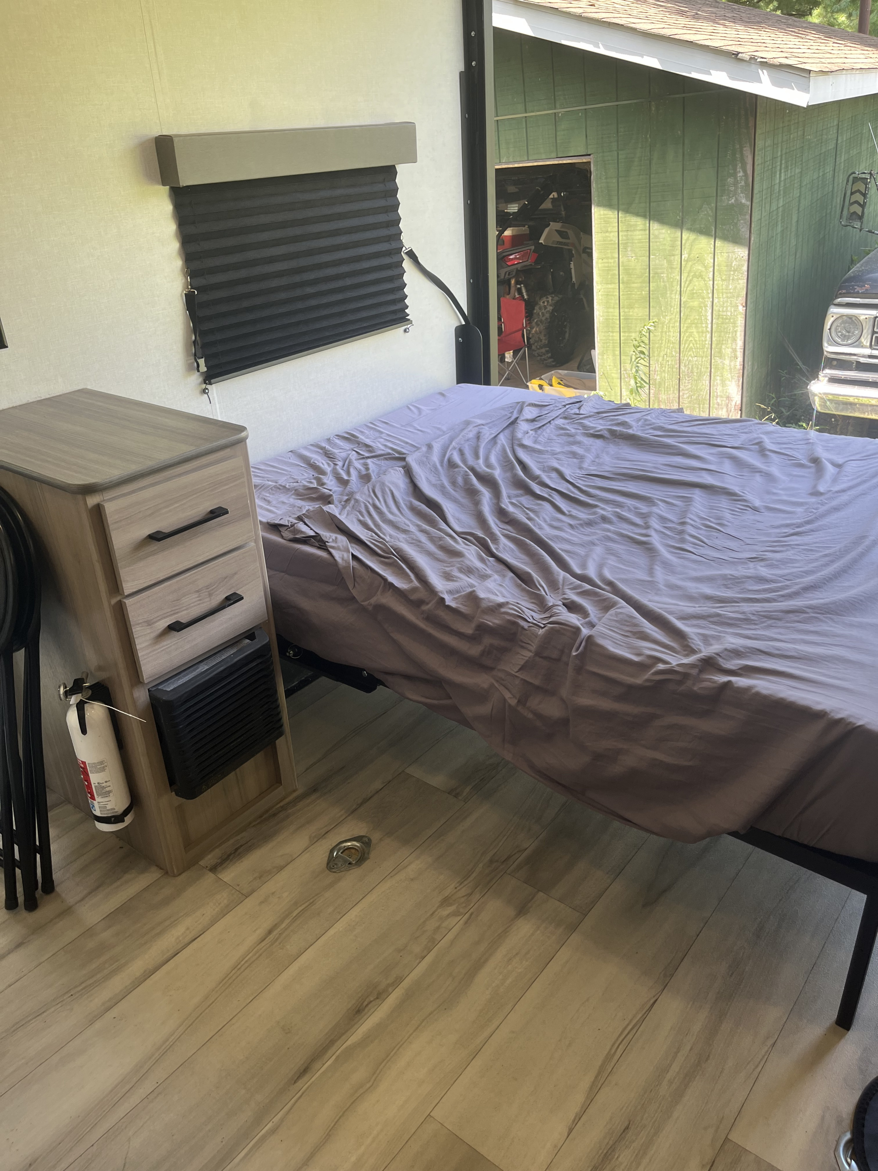 RV rental bedroom: Bed, nightstand with fire extinguisher, pleated blind, and outdoor view of a shed and ATV.. Keystone Coleman 13T 2026