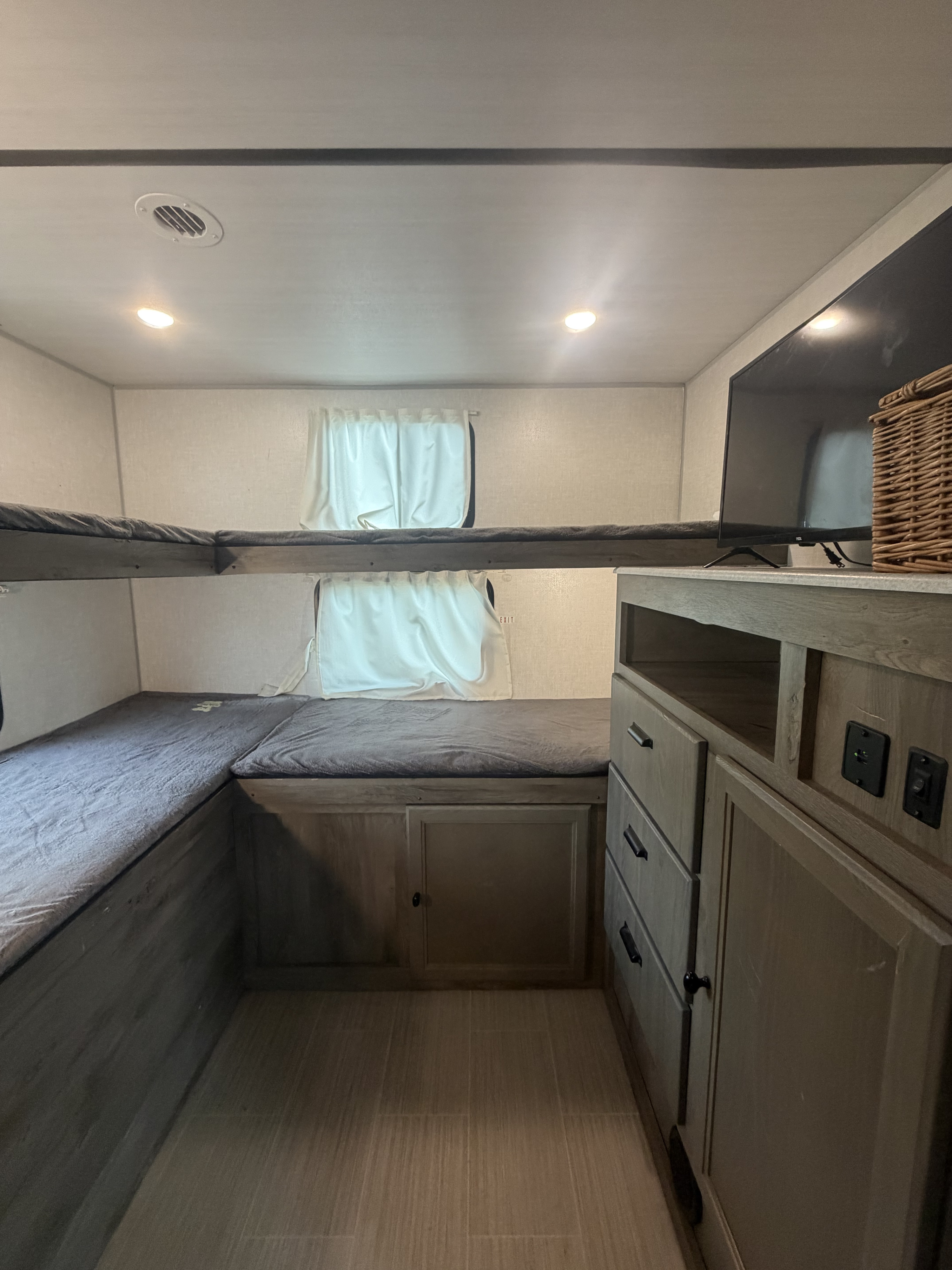 This RV rental interior features bunk beds with grey mattresses, built-in storage, a TV, and recessed lighting.. Forest River Surveyor Legend 2021