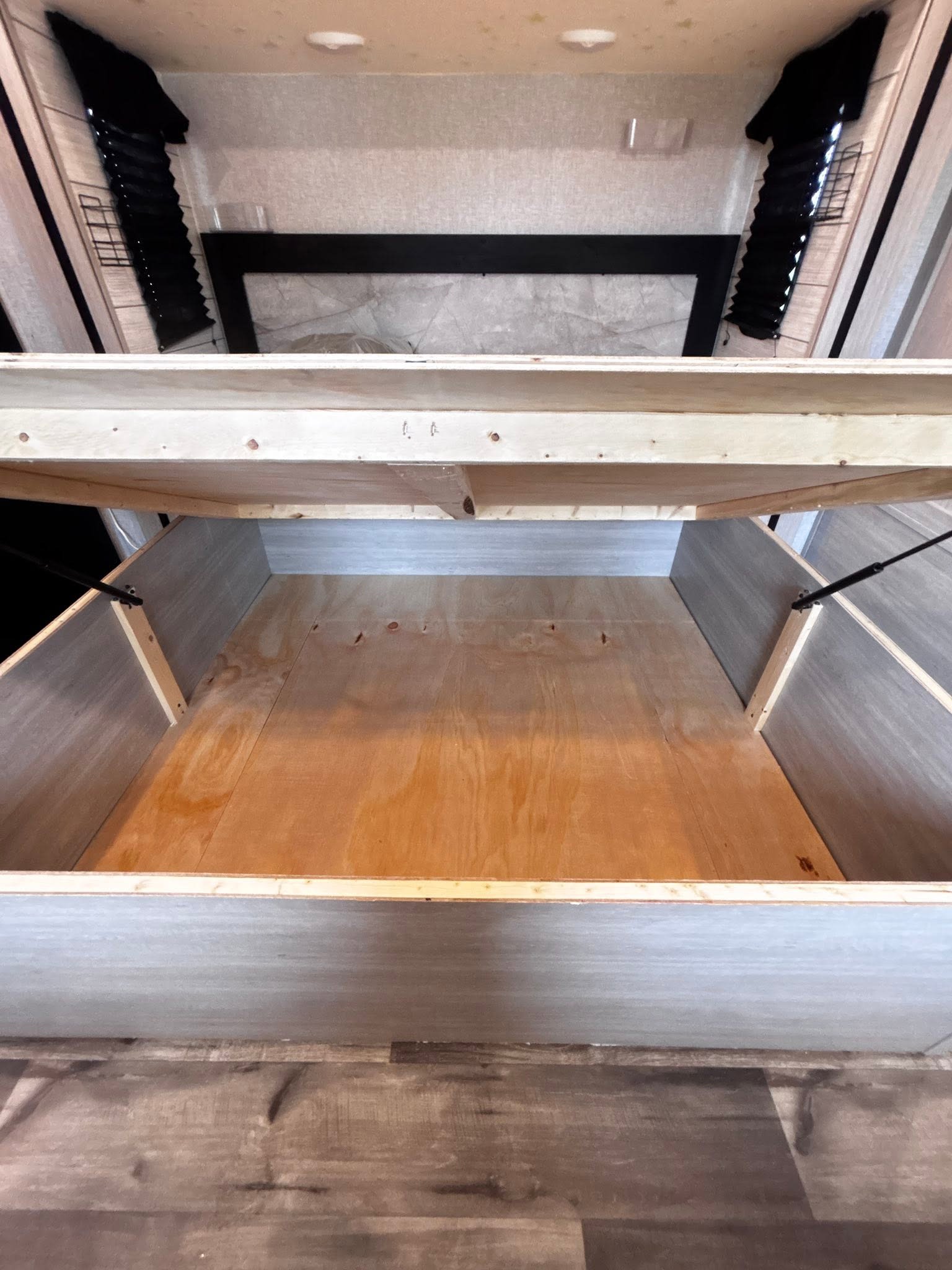 View into a spacious RV rental bed storage compartment, with the wooden platform lifted and gas struts visible, ready for travel.. Crossroads RV Sunset Trail Super Lite 2024