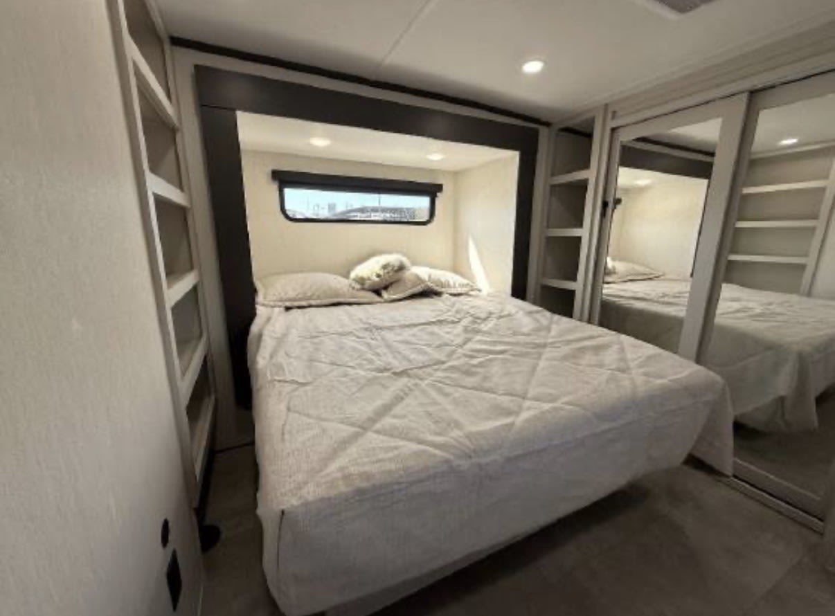 Inside an RV rental, this cozy bedroom features a bed with light bedding, a small window, built-in shelves, and mirrored closets.. Prime Time Rv Bonus 38 2027