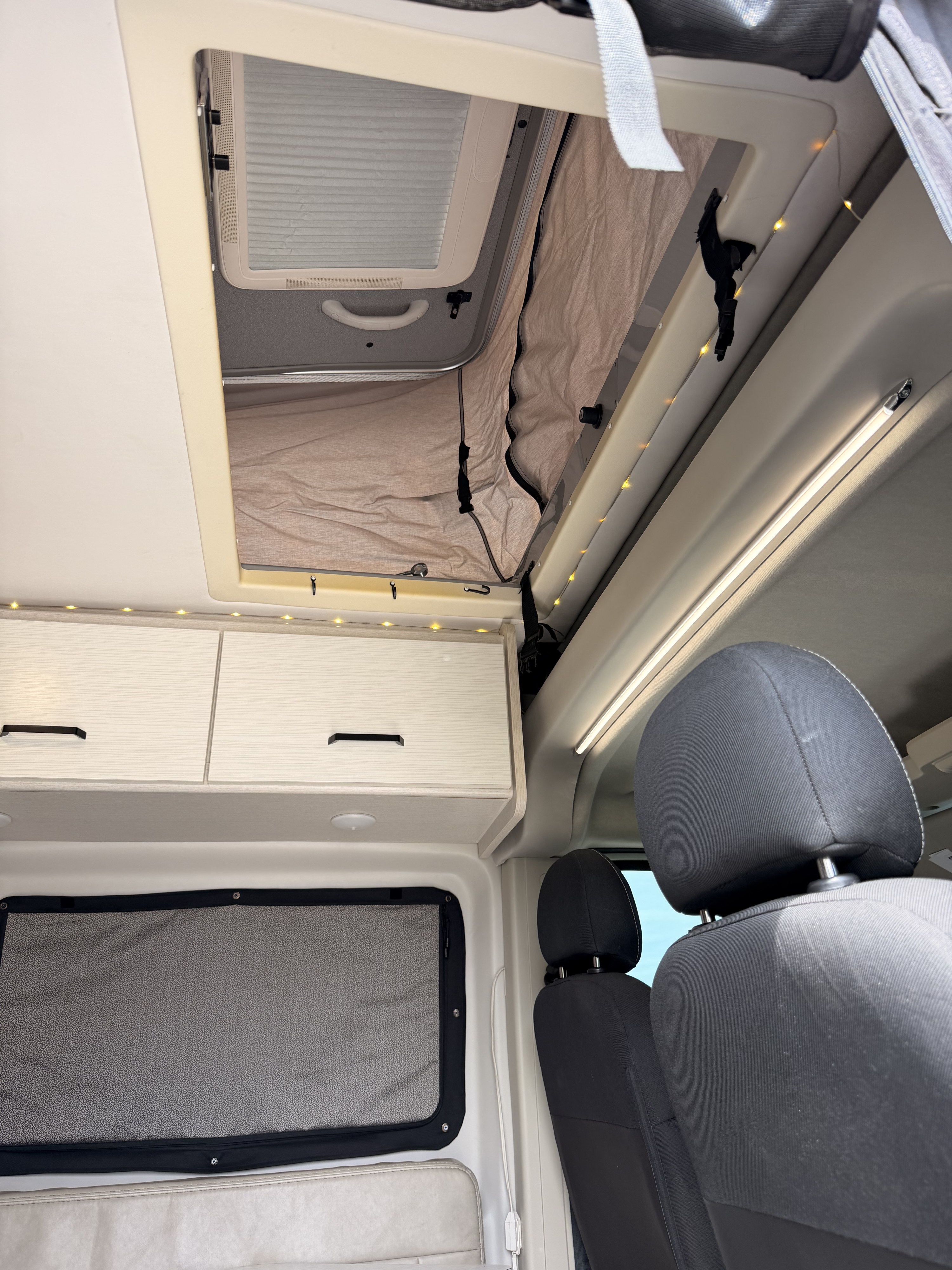 Interior of an RV rental, featuring a large pop-top roof with blinds, overhead cabinets, and ambient lights, plus passenger seating.. Dodge Ram 1500 2023