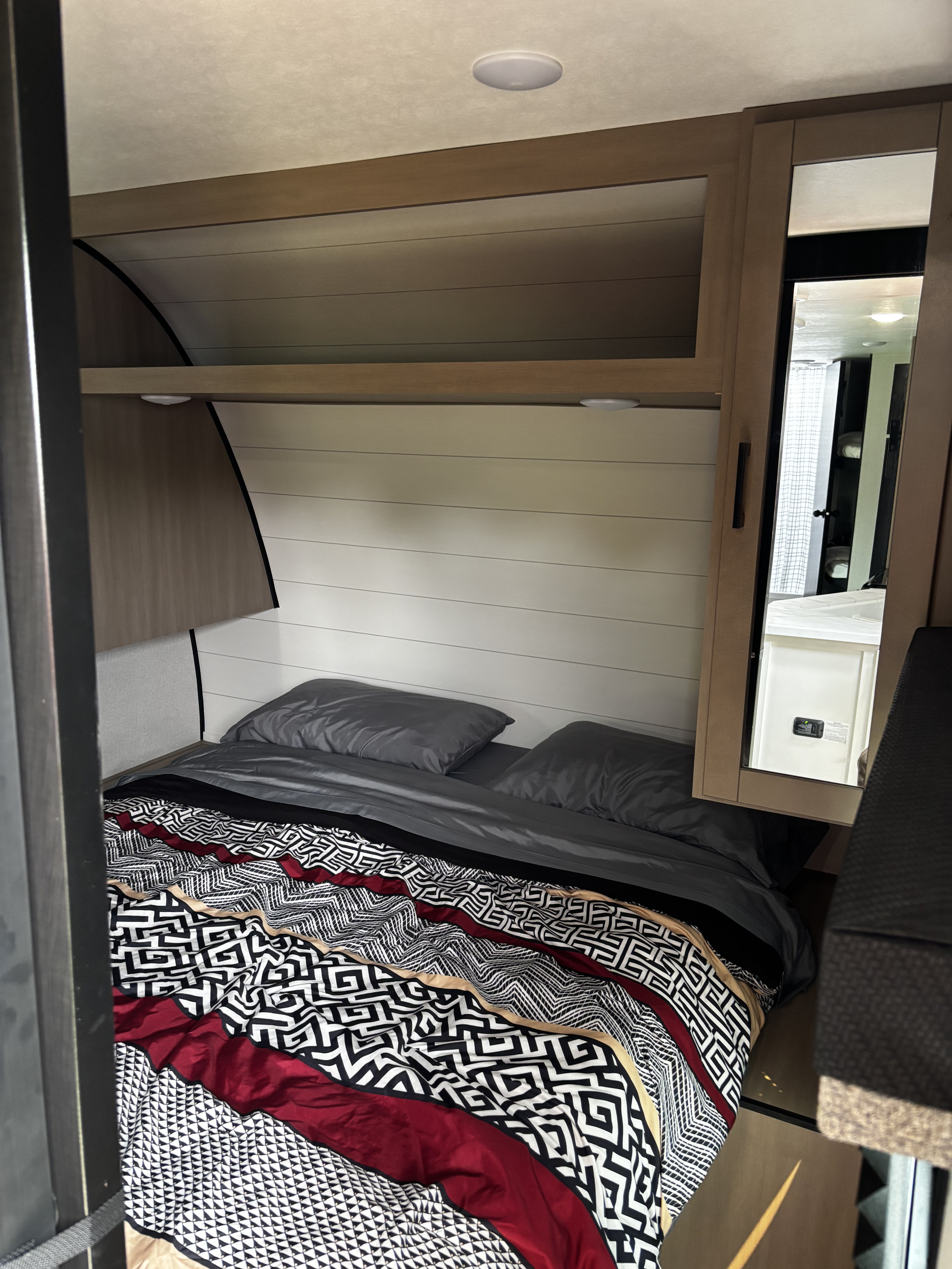 Cozy RV rental bedroom: comfortable bed with gray bedding, patterned comforter, overhead storage, and mirrored cabinet.. Starcraft Autumn Ridge 2026