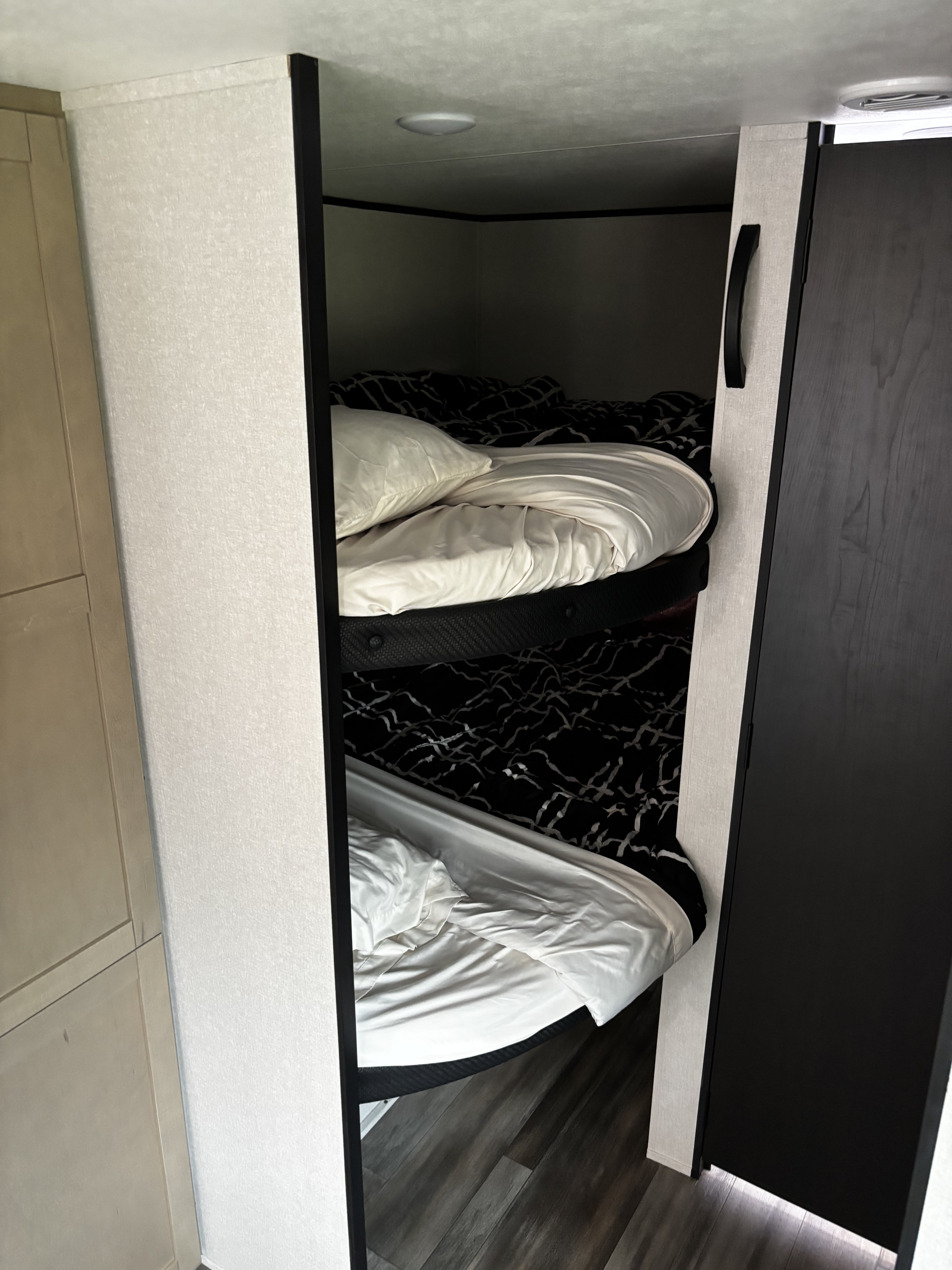 RV rental features stacked bunk beds. White pillows, sheets, and dark patterned blankets offer a cozy, compact sleeping area.. Starcraft Autumn Ridge 2026
