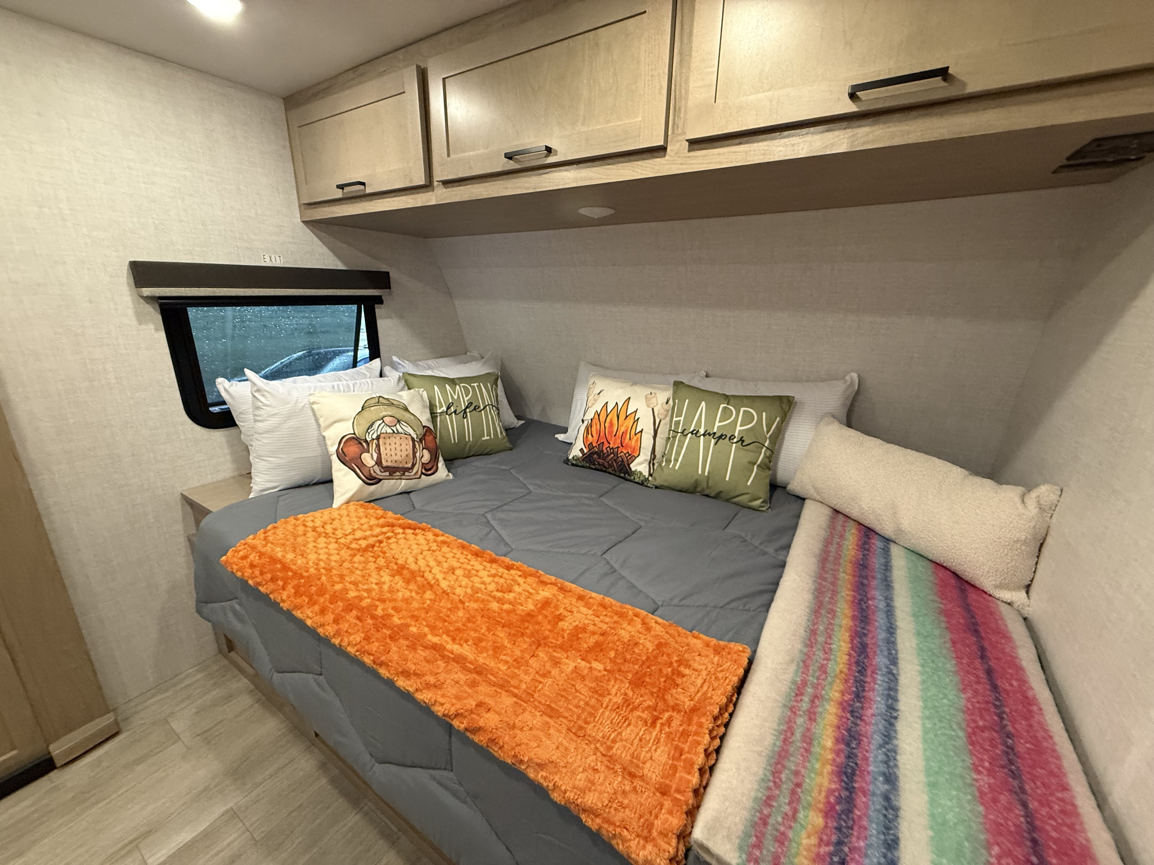 This cozy RV rental bedroom features a comfy bed with camping-themed pillows, overhead cabinets, and a welcoming ambiance.. Ember 19 ETS 2026