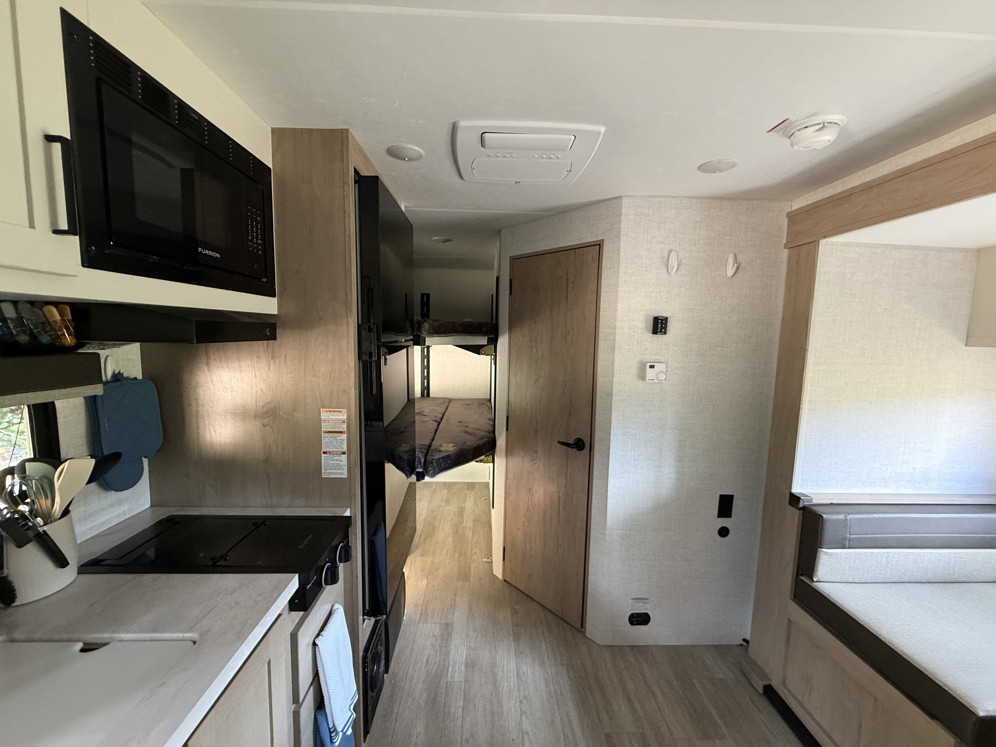 Inside an RV rental, featuring a full kitchen with microwave, stovetop, and sink, a dinette, and bunk beds visible down the hall.. Ember 19 ETS 2026