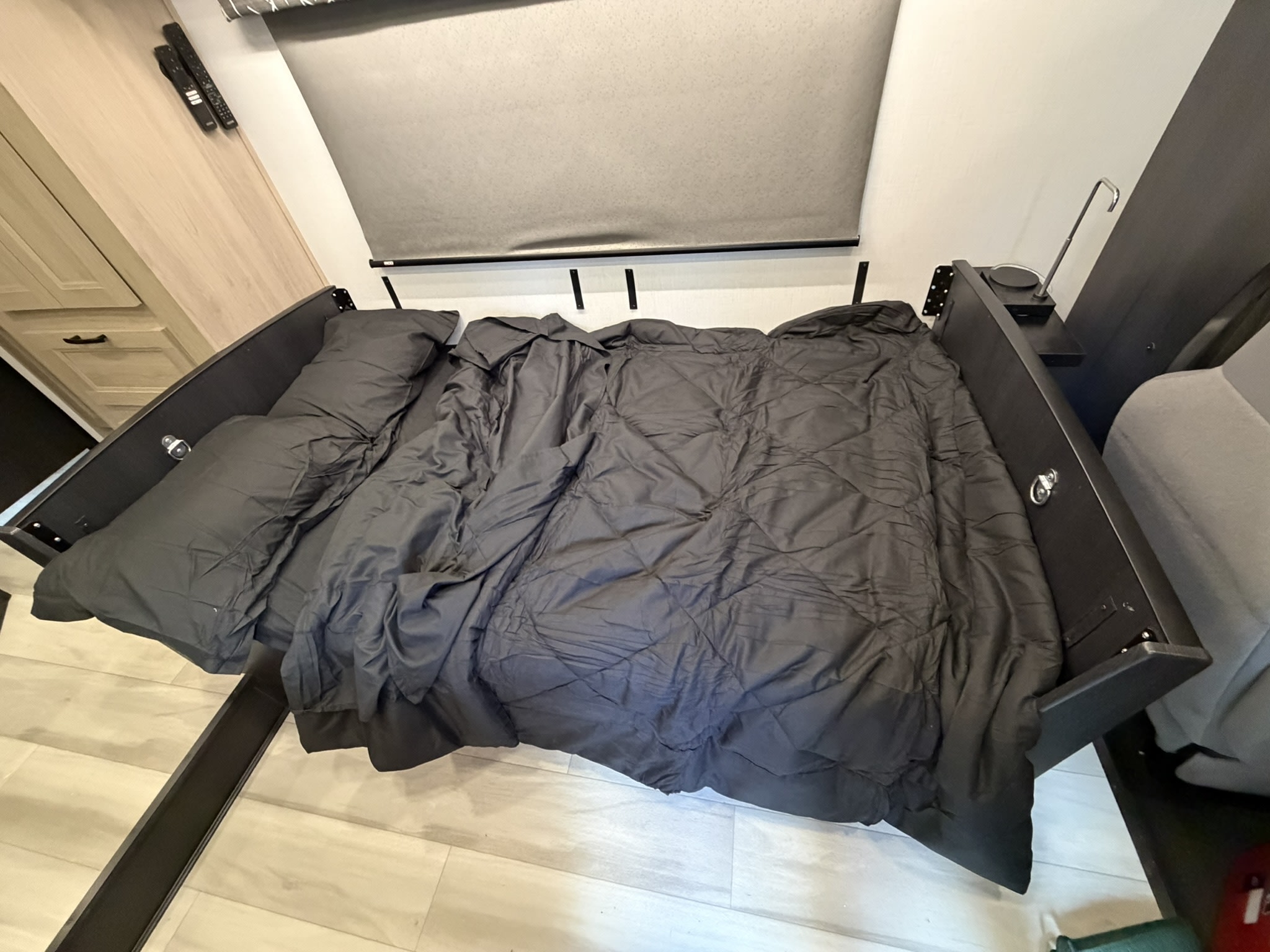 RV rental interior: a compact bed with dark bedding, window shade, and wall-mounted controls in the bedroom.. Forest River Sunseeker LE 2025