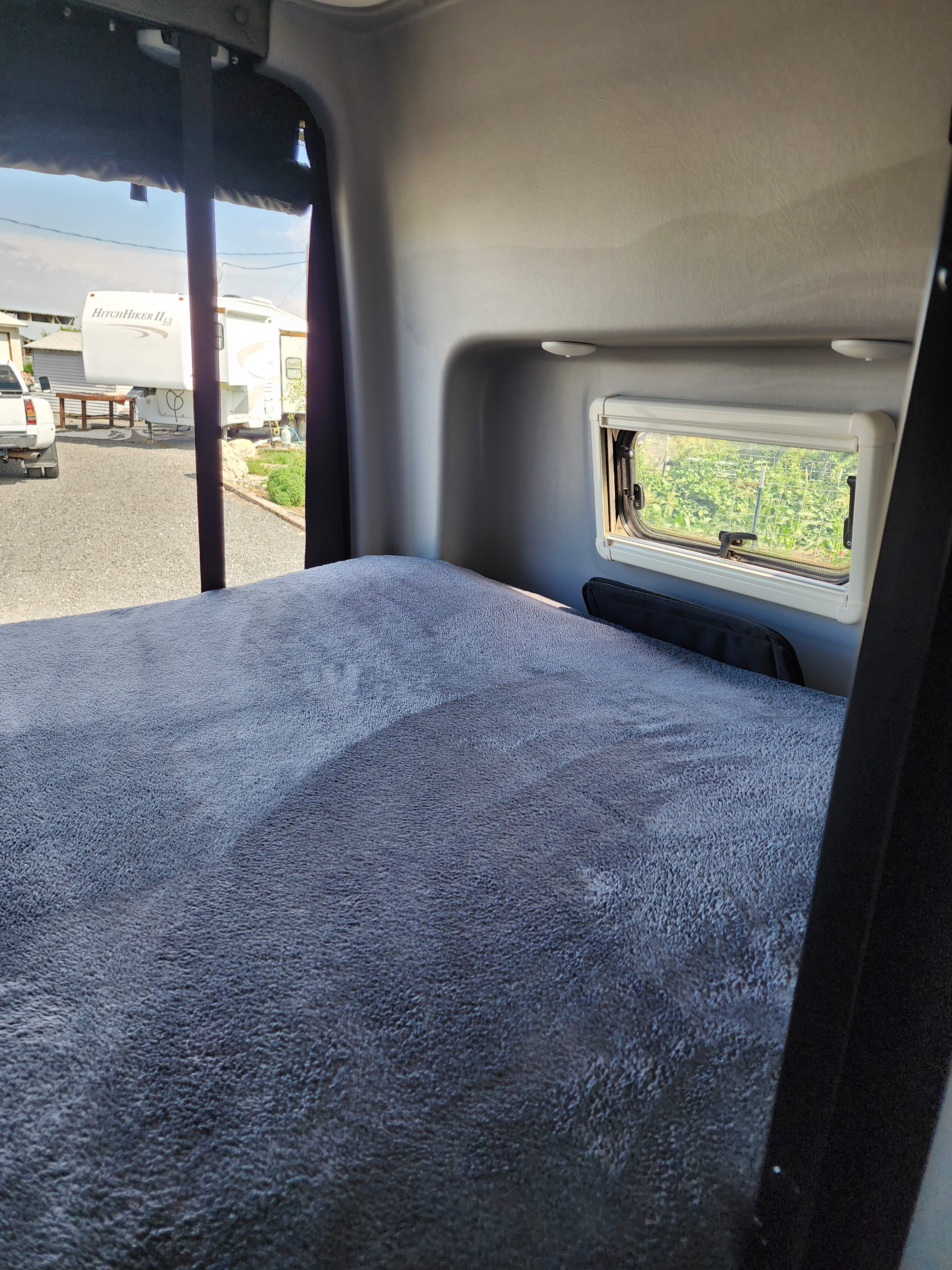 Cozy RV rental interior showing a comfortable bed, window, and a glimpse of the outdoor campsite.. Winnebago Revel 2021