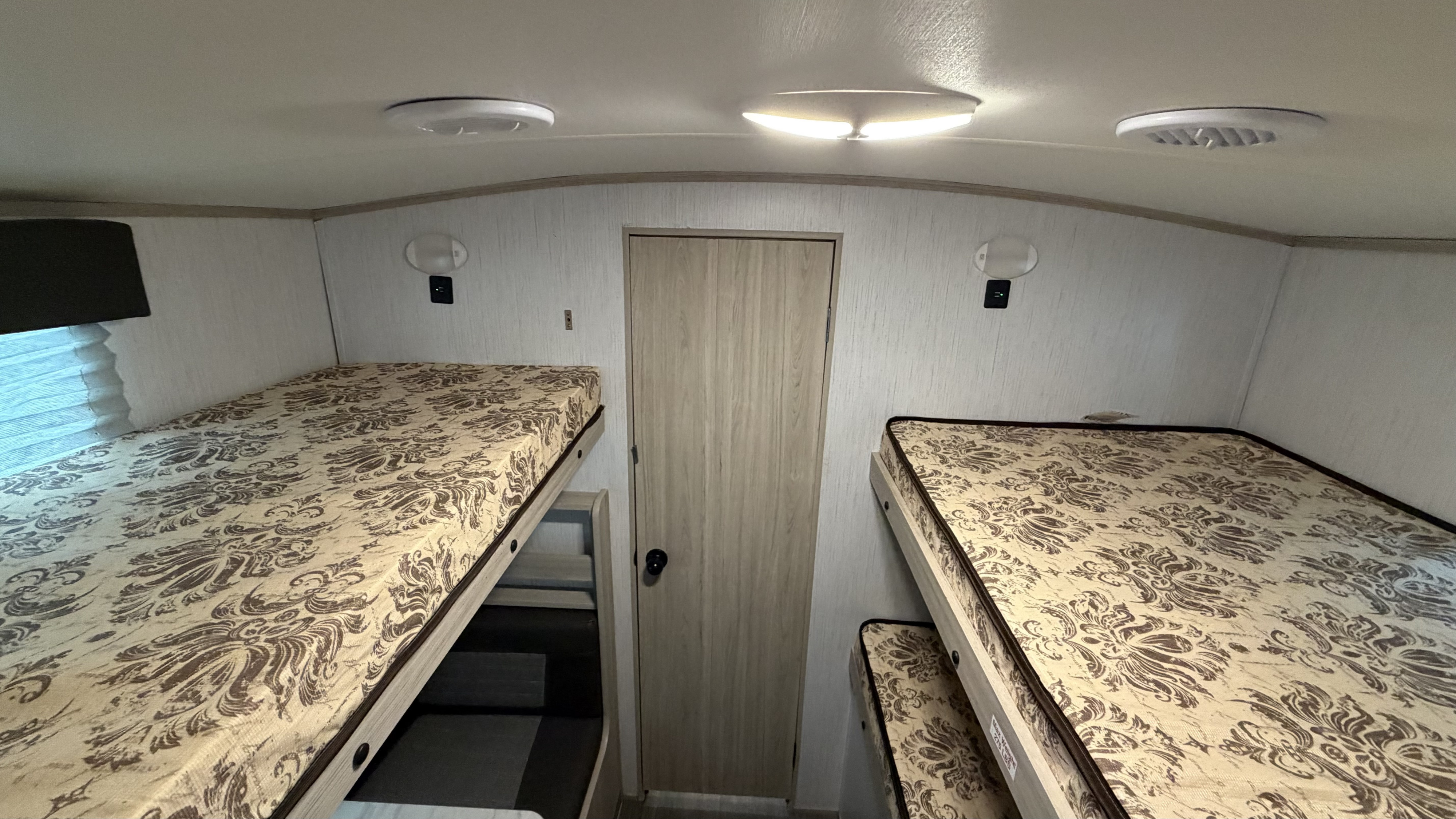 RV rental bunk bed area. Four bunks with patterned mattresses, ceiling lights, vents, and a door for cozy camper sleeping.. Cruiser RV Shadow Cruiser 2022