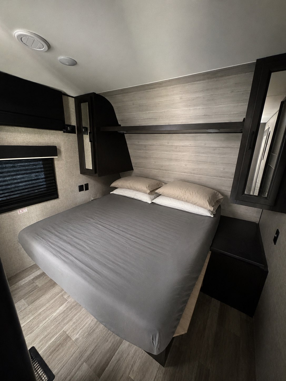 Comfortable rv rental bedroom: large bed with gray sheets, light wood-look walls, dark overhead storage, window with blind, and wood floor.. Jayco Jay Flight 2022
