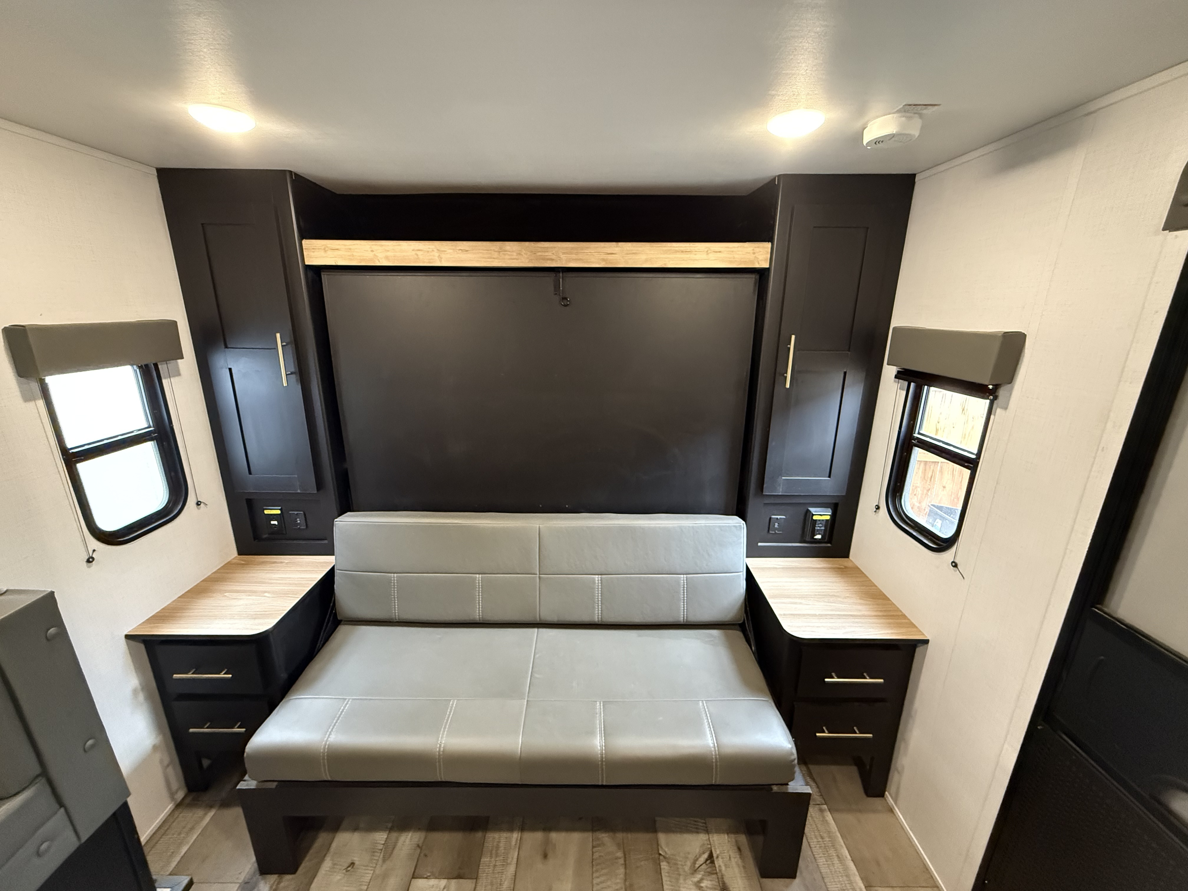 RV rental interior: a grey convertible sofa, dark overhead cabinets, and small side windows. Functional space for travelers.. Keystone RV Springdale 2023