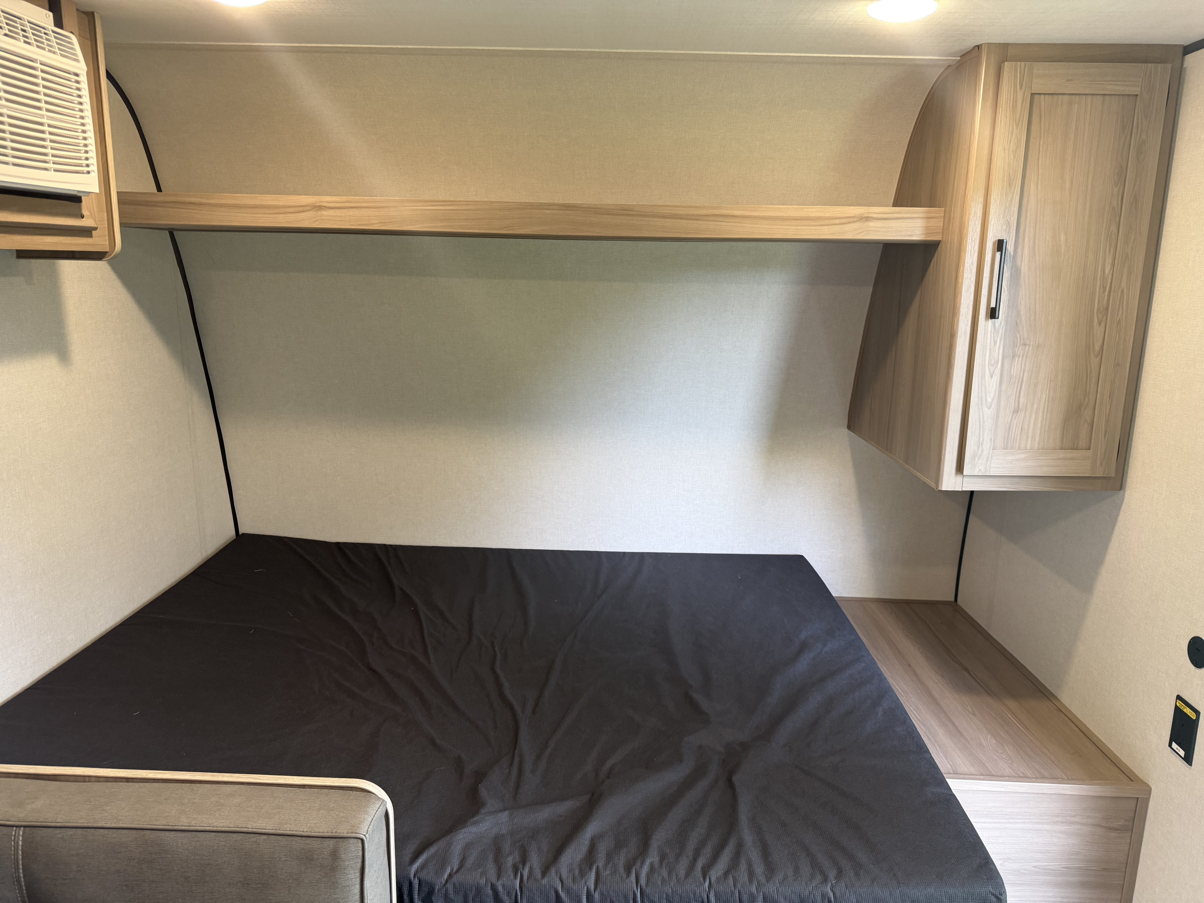 RV rental sleeping area: dark mattress, light wood shelving, AC unit, and electrical outlets for a cozy stay.. Keystone RV Coleman 2025