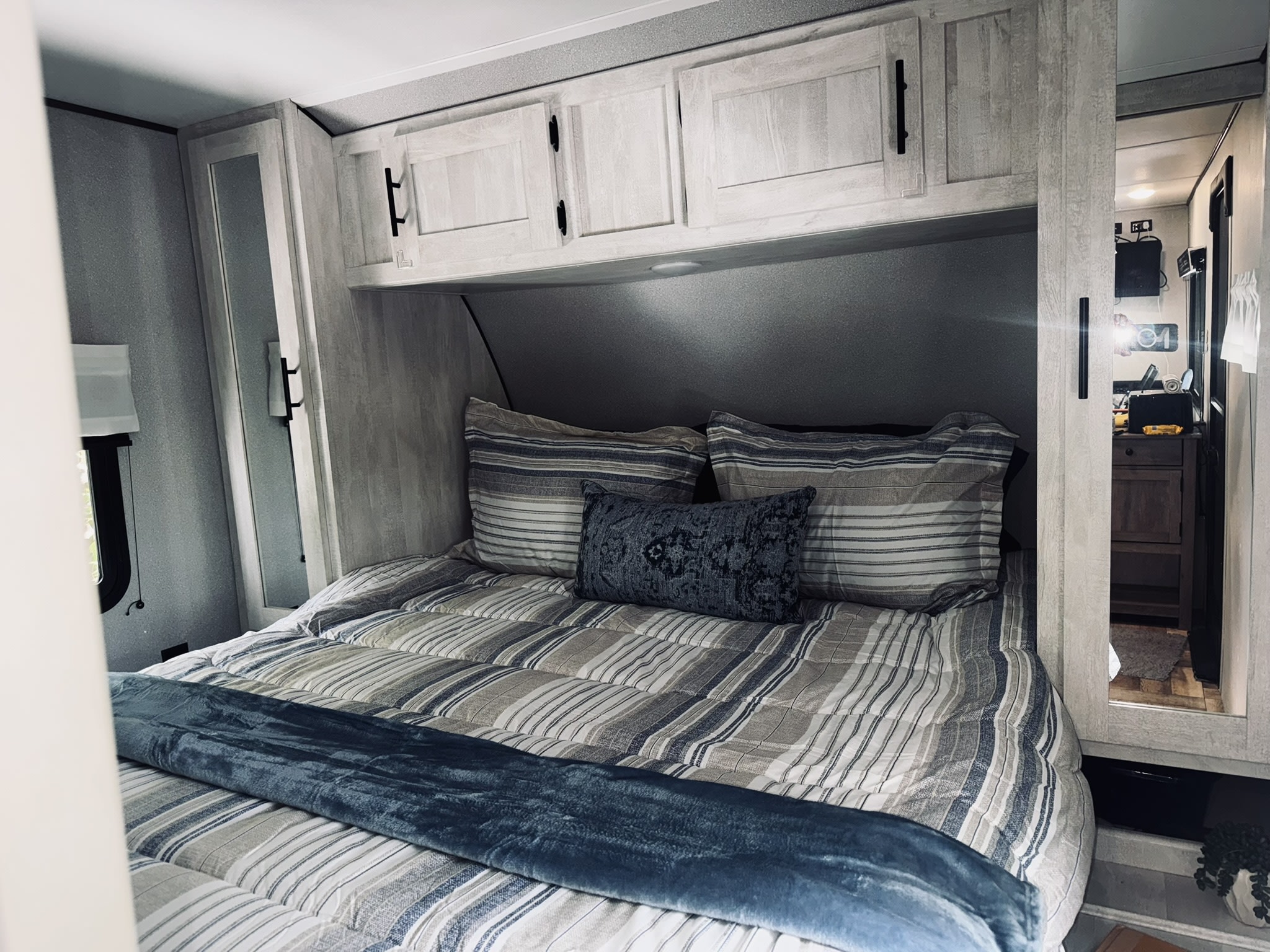 This RV rental bedroom features a neatly made bed with striped bedding, a blue throw blanket, and overhead storage cabinets.. Forest River Shasta 2022