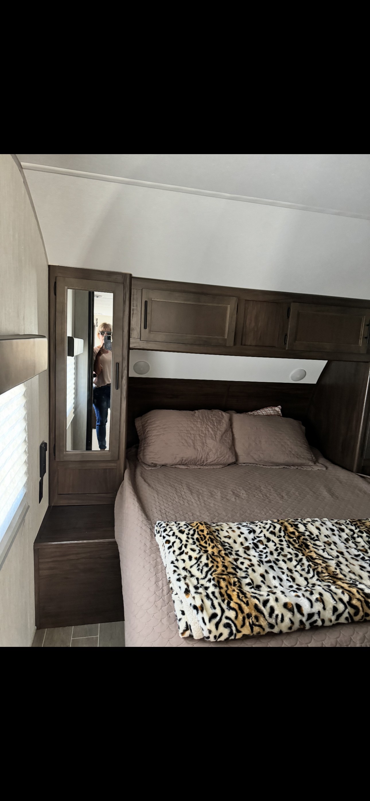 Cozy RV rental bedroom featuring a queen bed with leopard print blanket, built-in storage, and a mirror.. Forest River Cherokee 2021