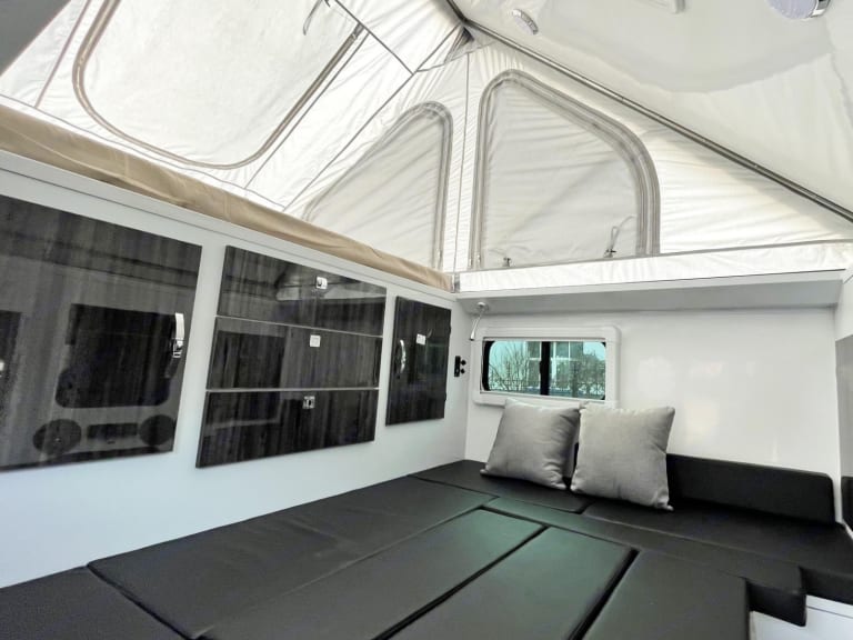 Modern rv rental interior: pop-top camper with convertible bed/seating, storage cabinets, & window. Ready for your adventure.. Zoomies Campers Spirit 2025