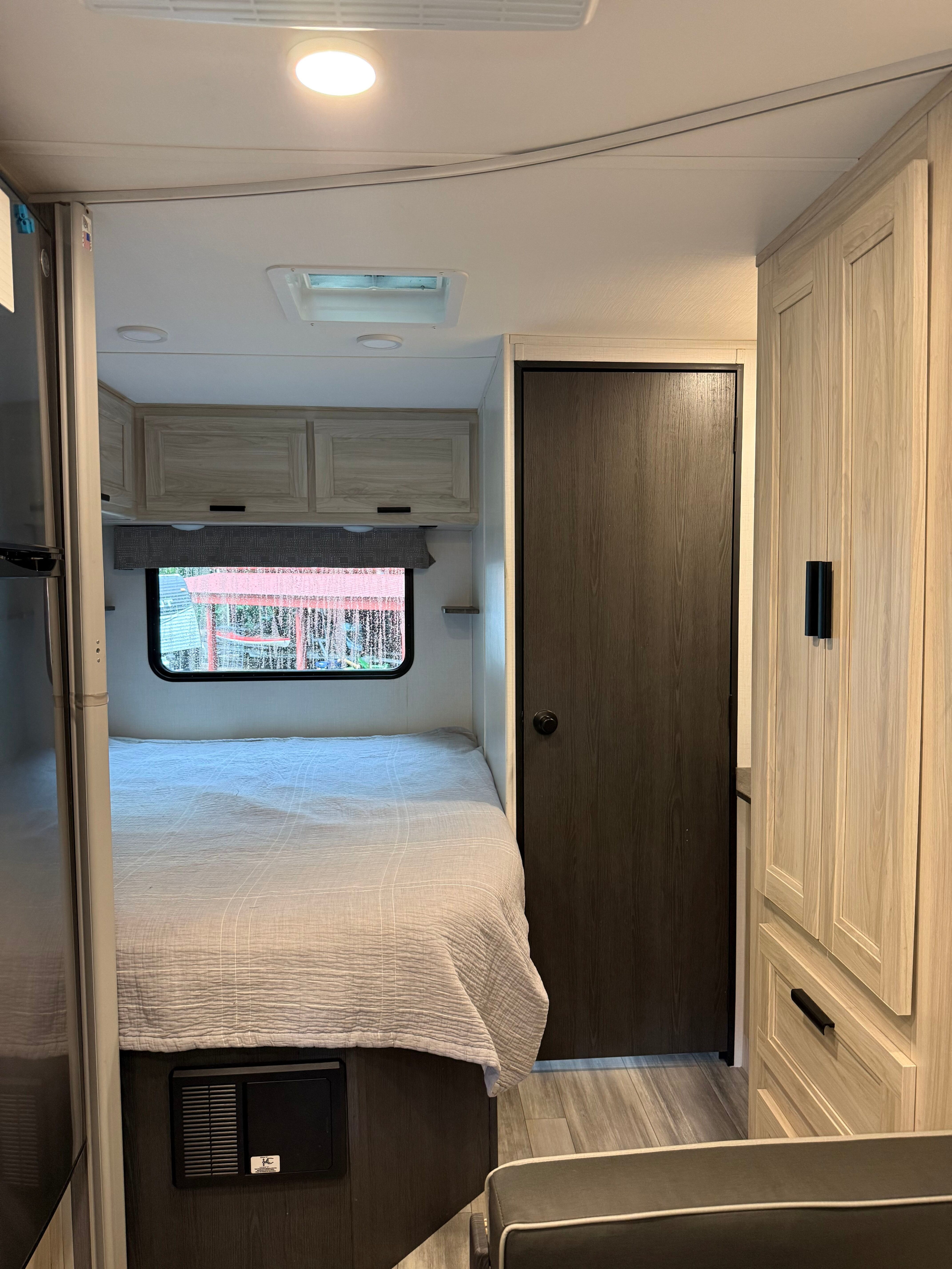 Explore this RV rental's cozy bedroom featuring a comfortable bed, light-toned cabinets, and a dark wood door, ideal for travel.. Forest River Sunseeker LE 2023