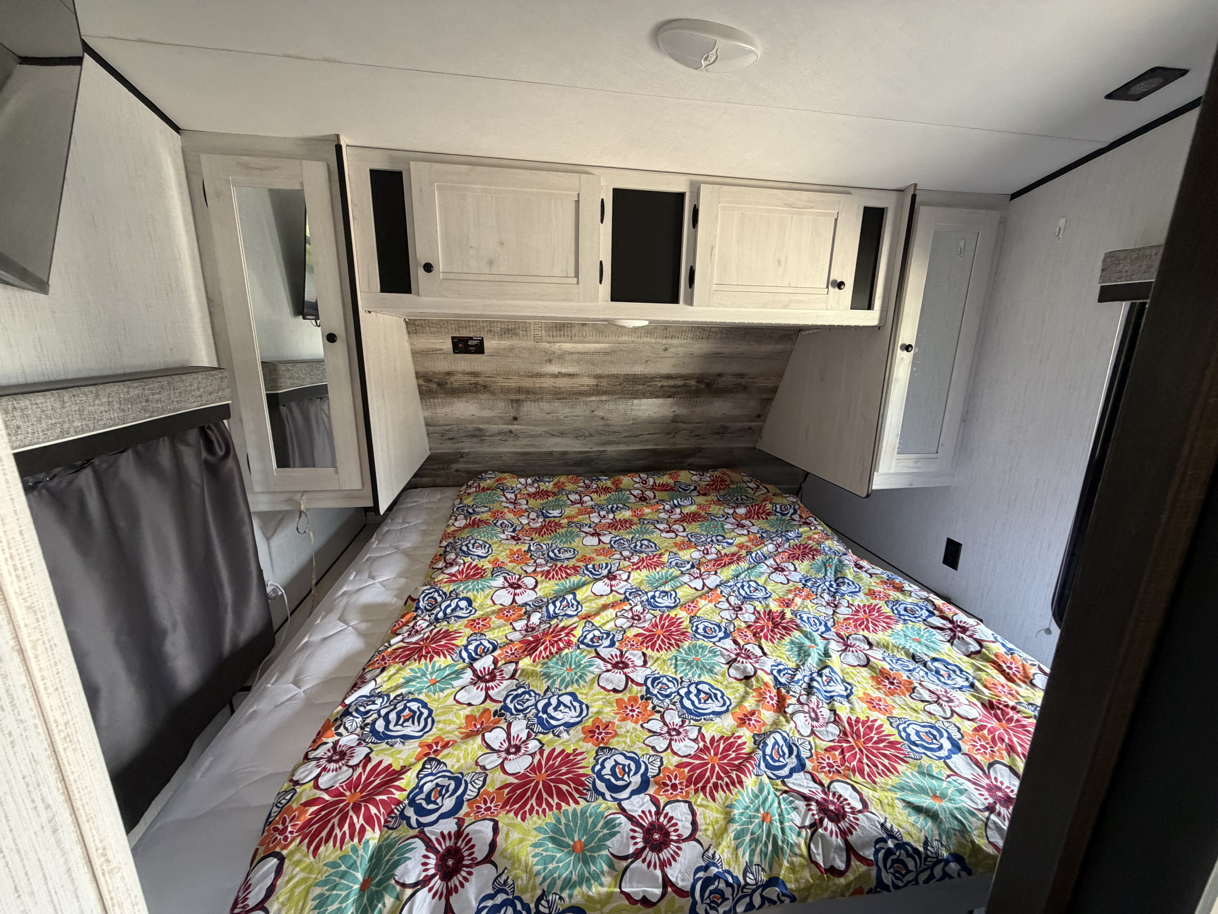 Cozy RV rental bedroom featuring a bed with a bright floral comforter, light wood cabinetry, and overhead storage.. Heartland Lithium 2021