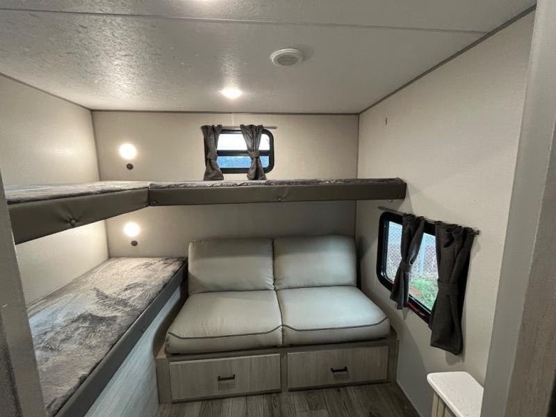 RV rental interior shows a compact bunkhouse: two beds, reading lights, and a small sofa with storage.. Forest River Catalina Coachmen Legacy 293QBCK 2026