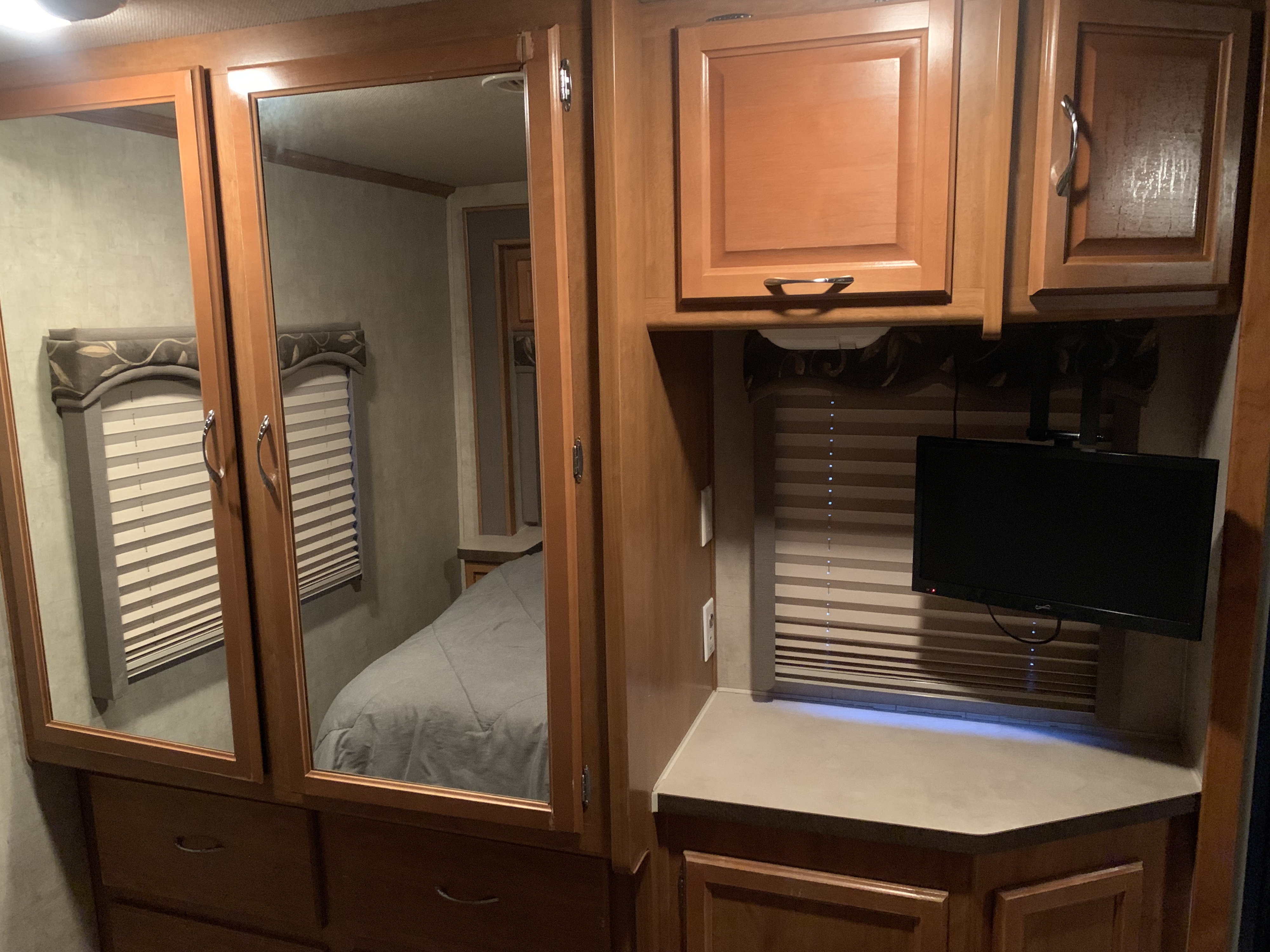 This RV rental bedroom features mirrored wardrobes reflecting a bed & window blinds, plus a mounted TV & wooden cabinets for storage.. Jamboree Jamboree Motorhome 2006