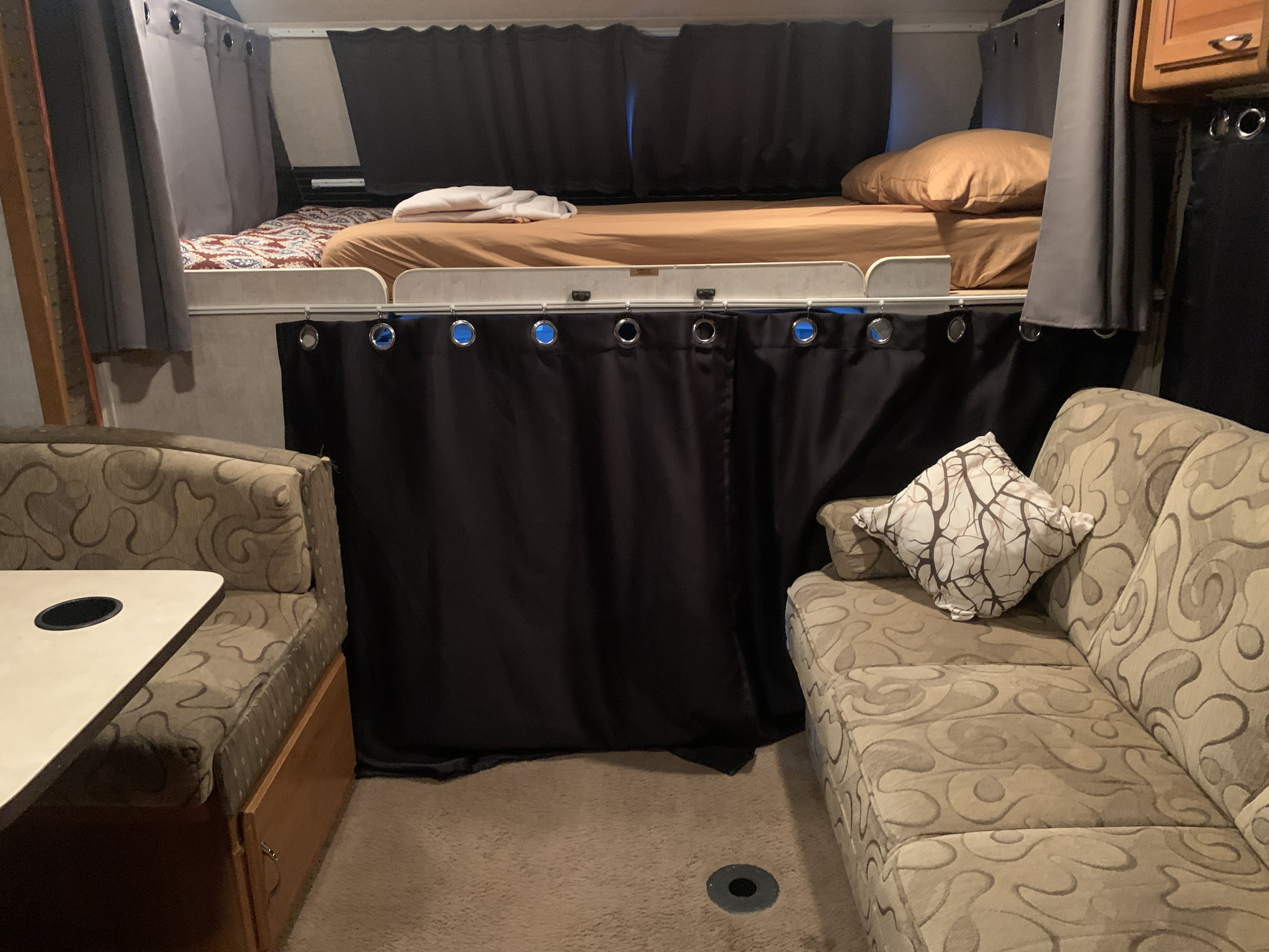 RV rental interior features a raised bed with privacy curtains, a dinette, and comfy patterned seating.. Jamboree Jamboree Motorhome 2006