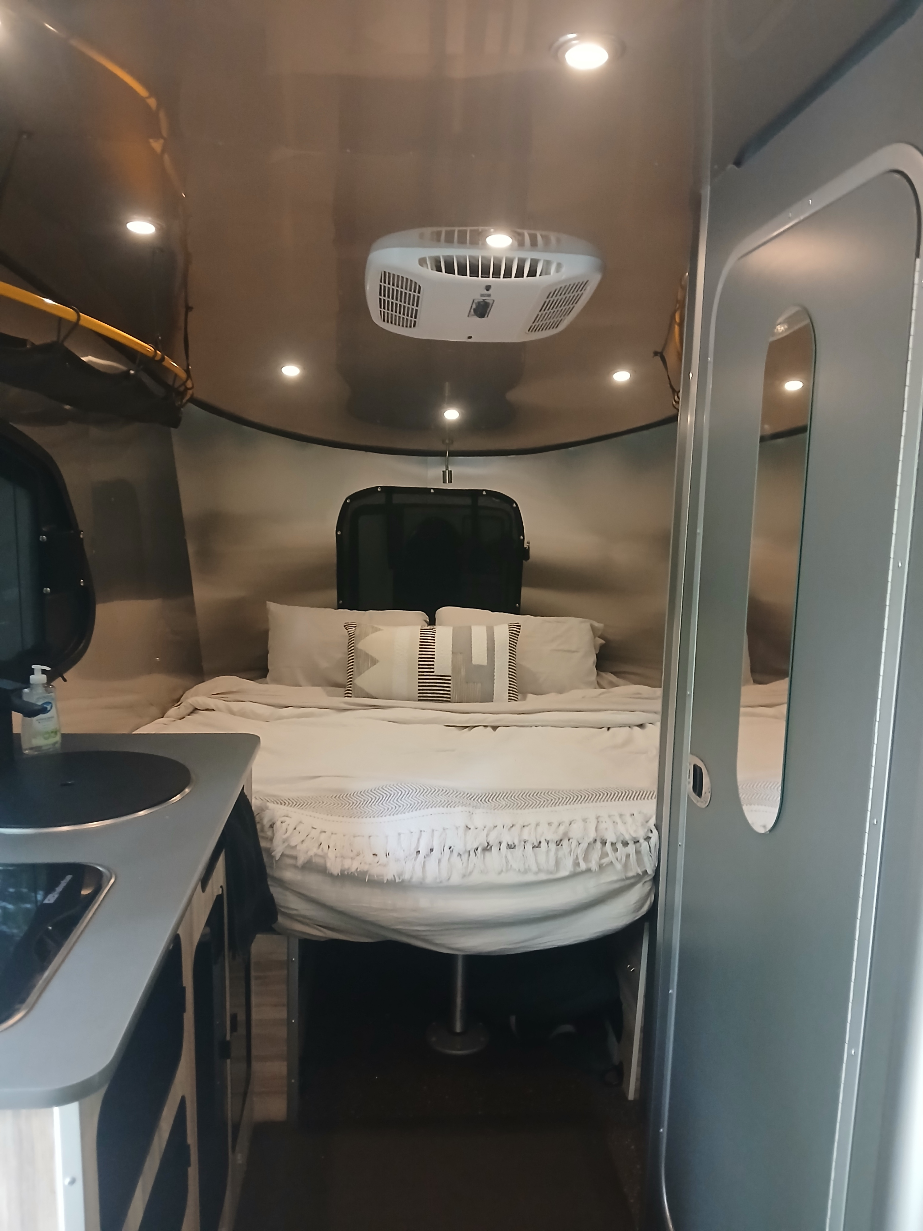 Cozy interior of an **rv rental** showing a comfortable bed, overhead AC unit, and a compact kitchen counter. Ideal for travel.. Airstream Basecamp 2022