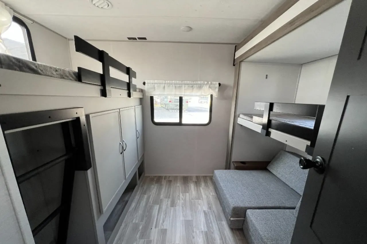 An RV rental interior with bunk beds on both sides, a gray modular sofa, storage cabinets, and a window, creating a compact living space.. Forest River Vibe 2024