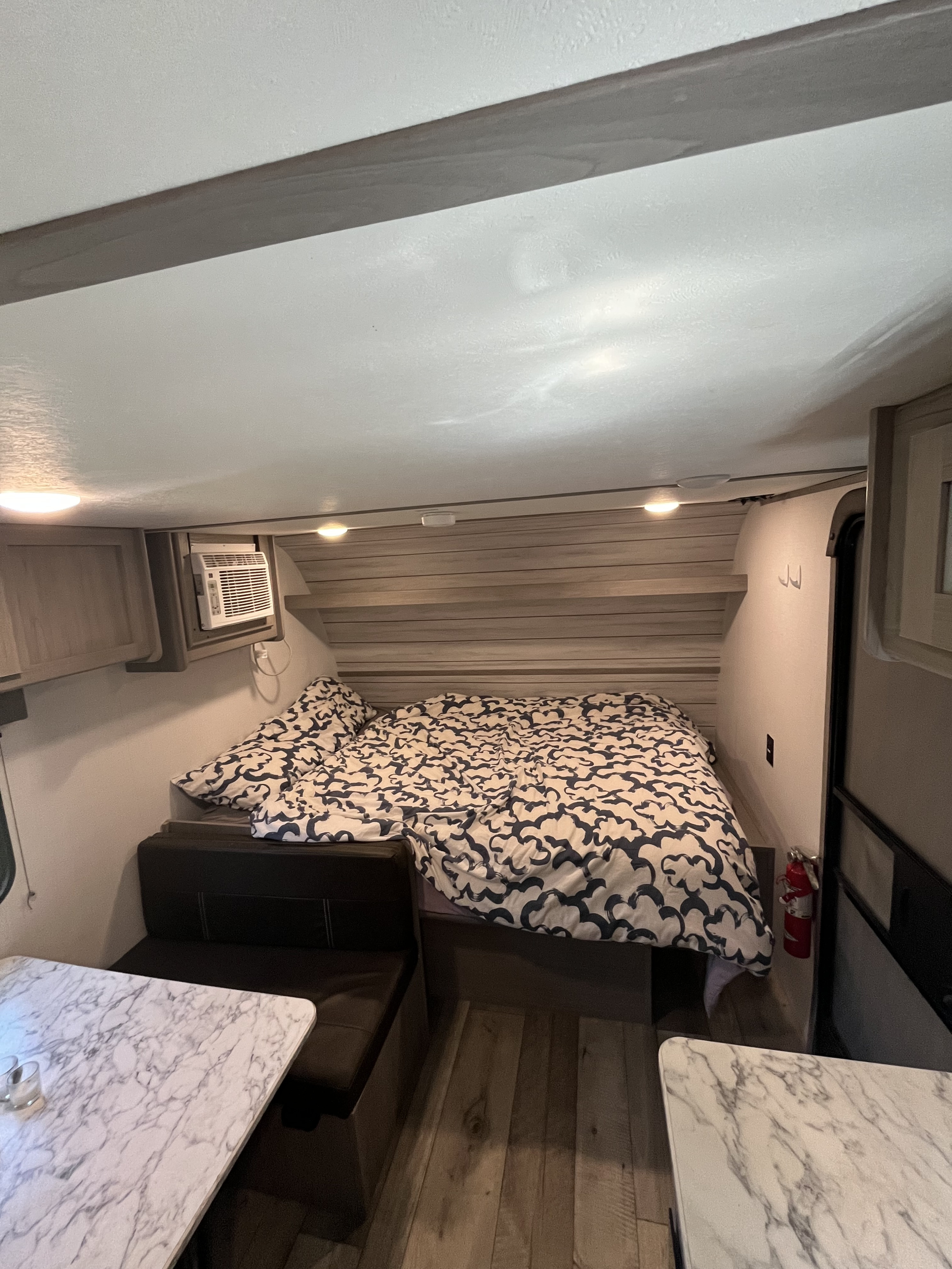 Cozy rv rental interior with a bed, patterned duvet, compact AC unit, and dinette seating with marble-look tables.. Coachmen 17b 2024