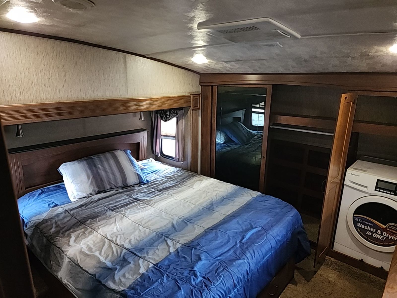 Comfortable RV rental bedroom with a striped bedspread, mirrored closet, and a Dometic washer/dryer. Enjoy travel amenities!. Forest River SABRE 2015