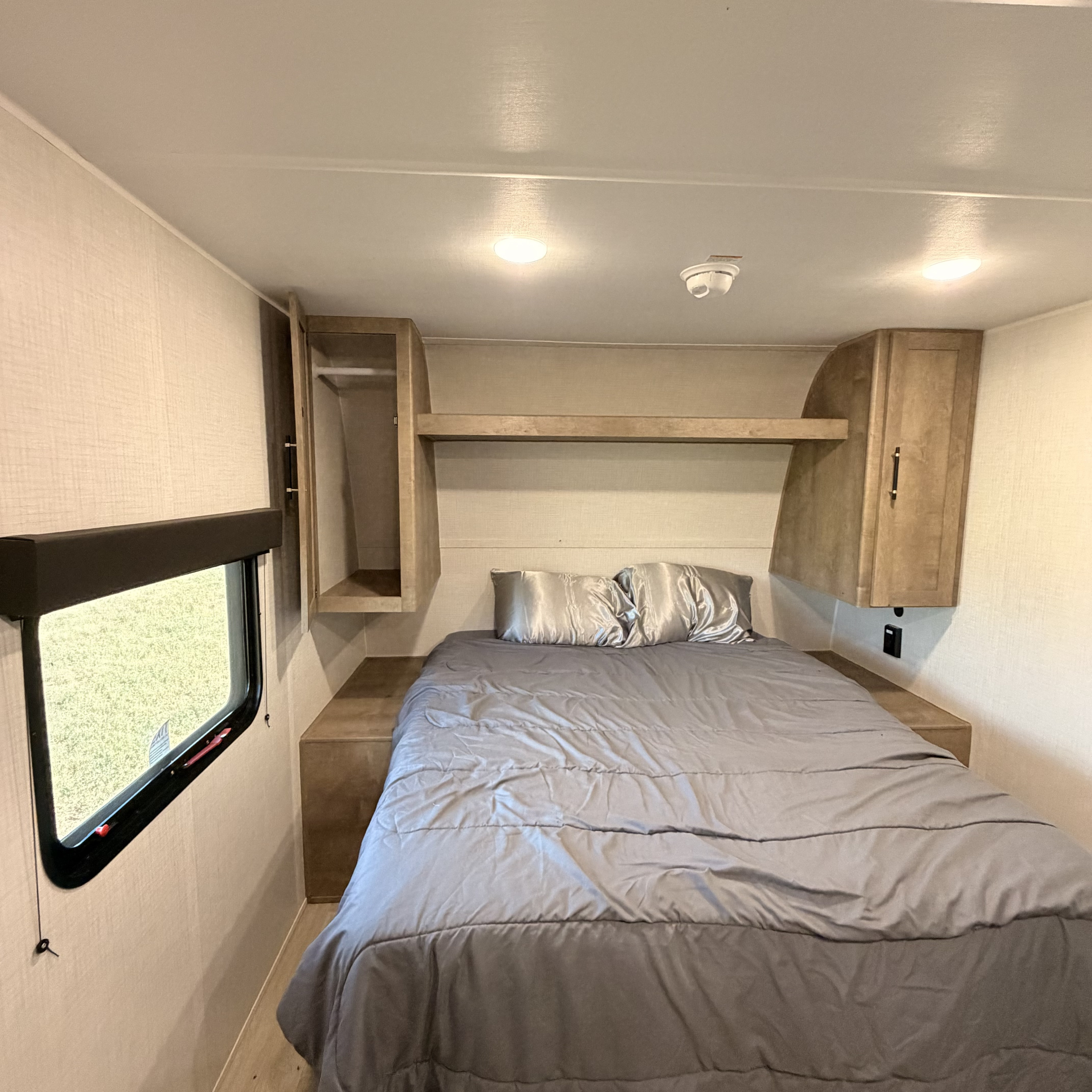 Step into this comfortable RV rental bedroom, featuring a large bed, built-in overhead storage, and a side window.. Keystone RV Springdale Mini 2026