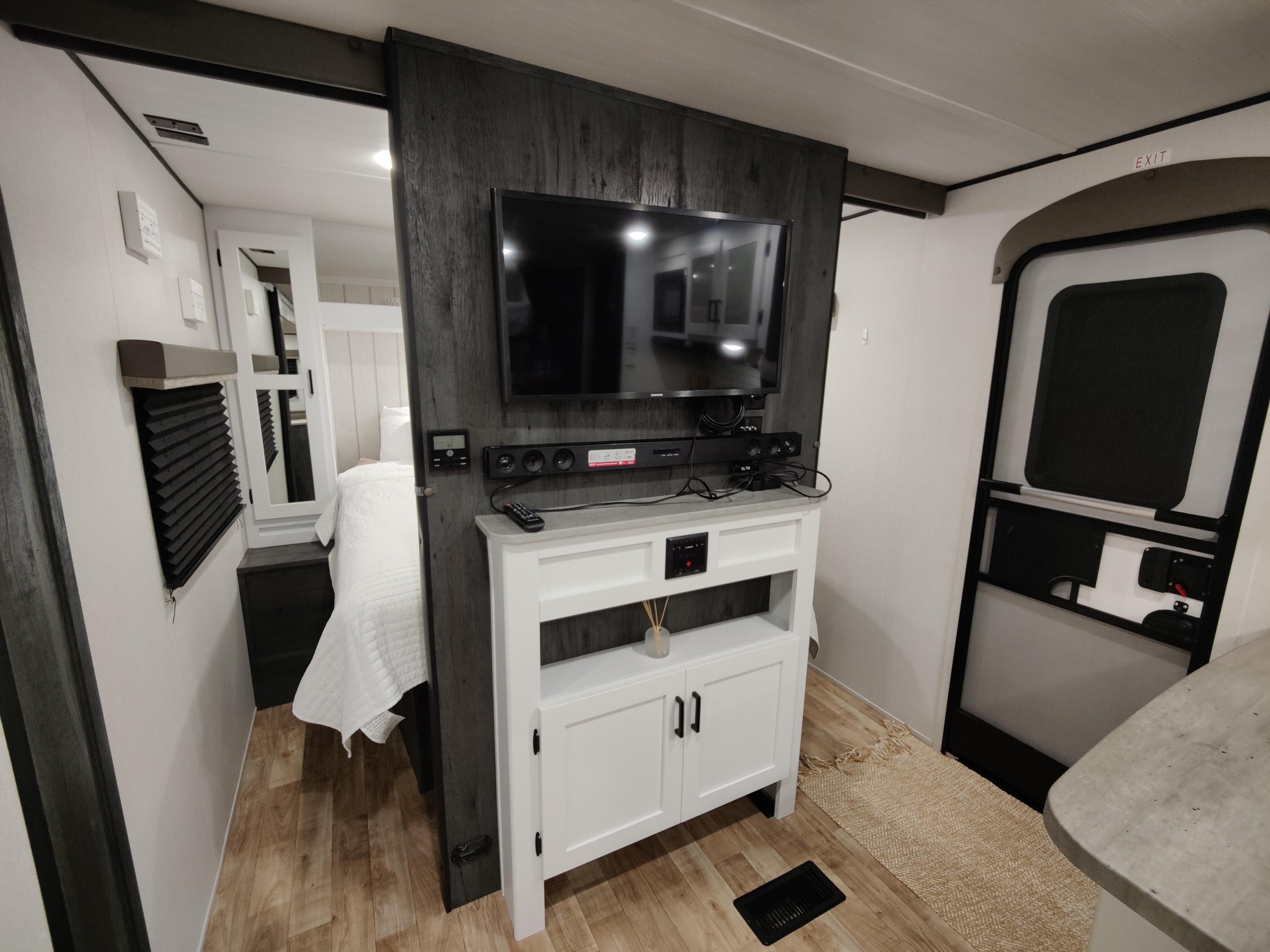 Modern RV rental interior: A compact living area with TV, soundbar, and console, peeking into the bedroom, by the exit door.. Keystone RV Hideout 2023