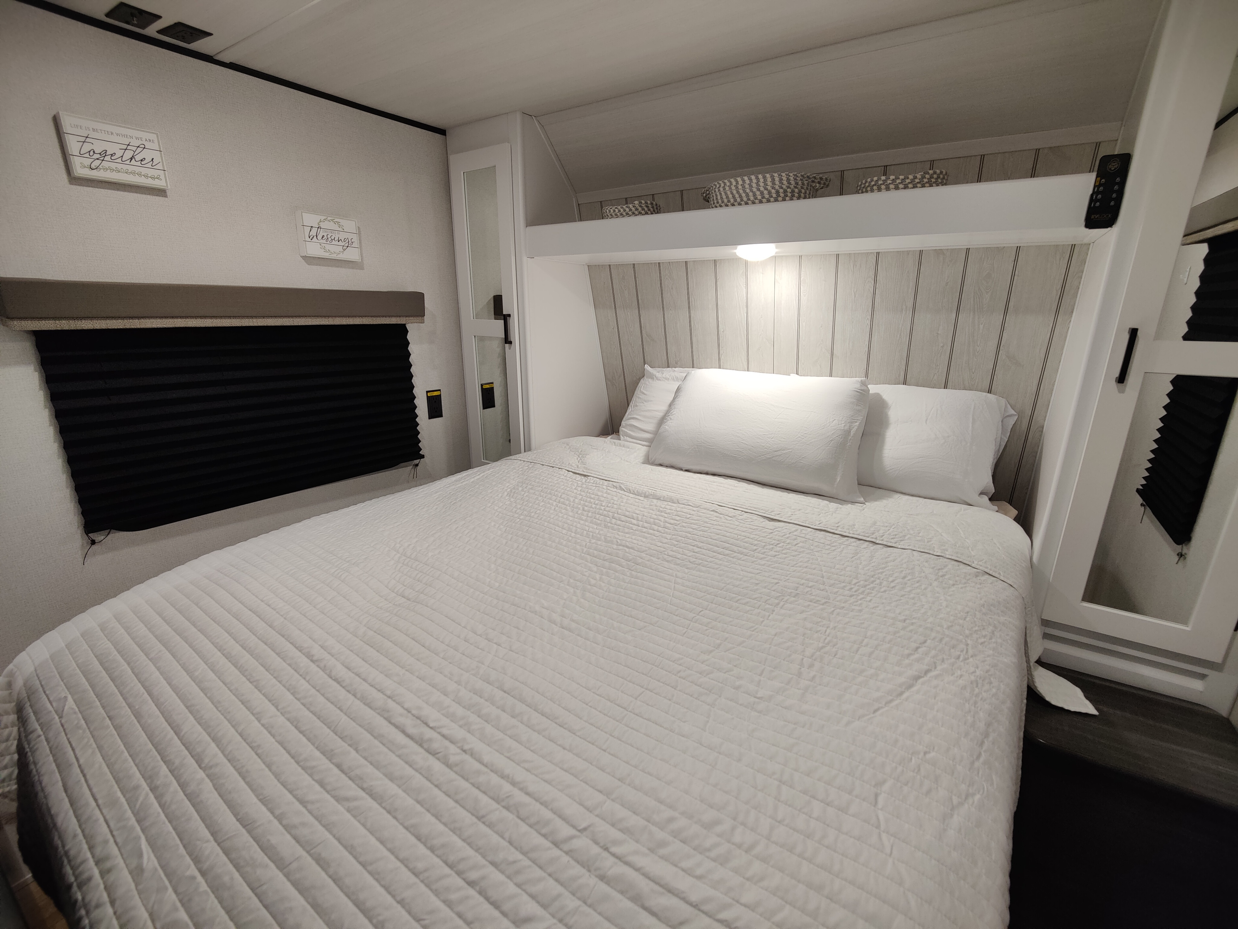 Inside this RV rental, find a bright bedroom with a plush white bed, wood-paneled headboard, and window with blinds.. Keystone RV Hideout 2023