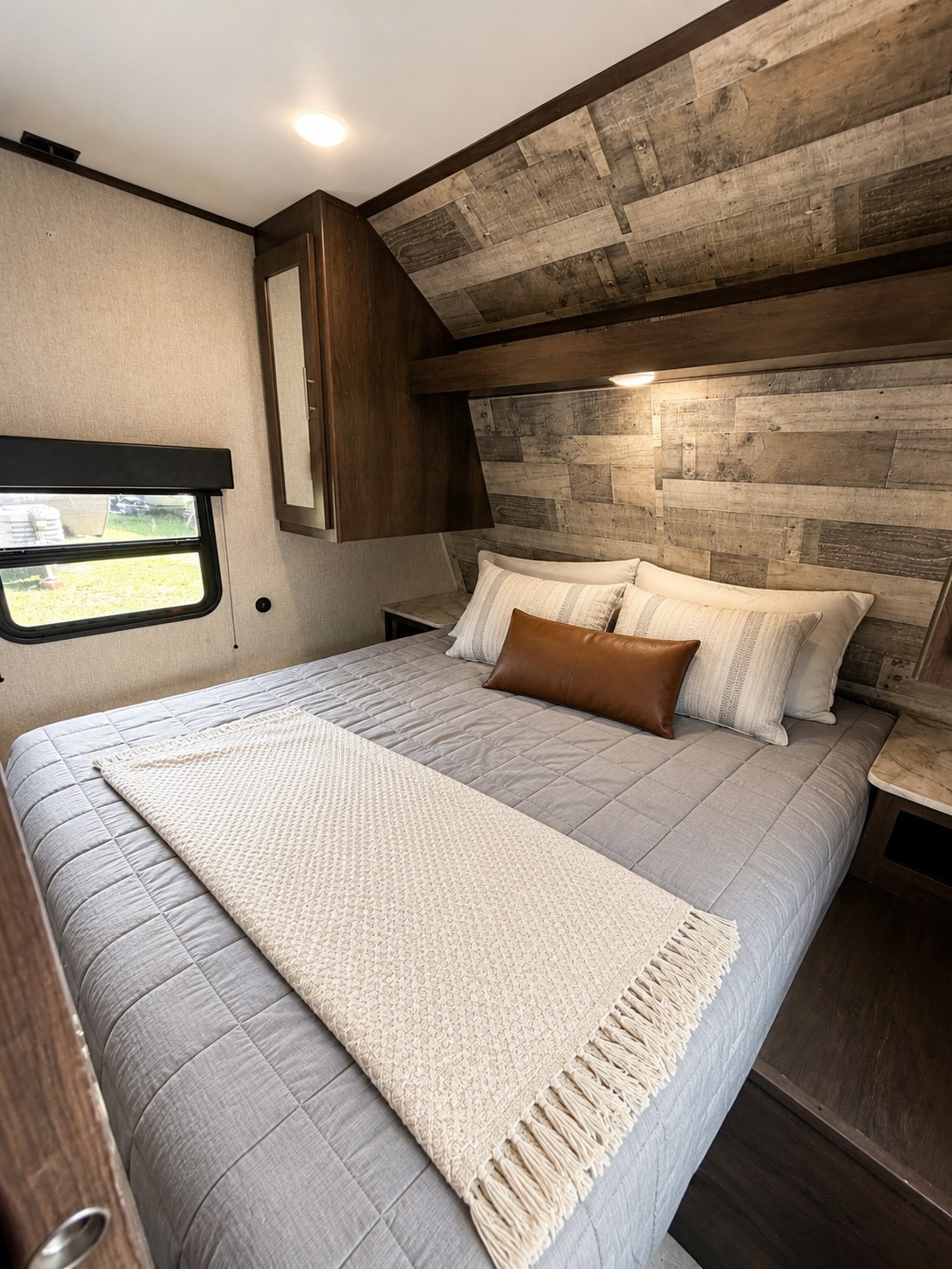 This cozy RV rental bedroom features a comfy bed with grey bedding, rustic wood paneling, and overhead storage, perfect for travel.. Dutchmen Coleman Lantern LT 2021
