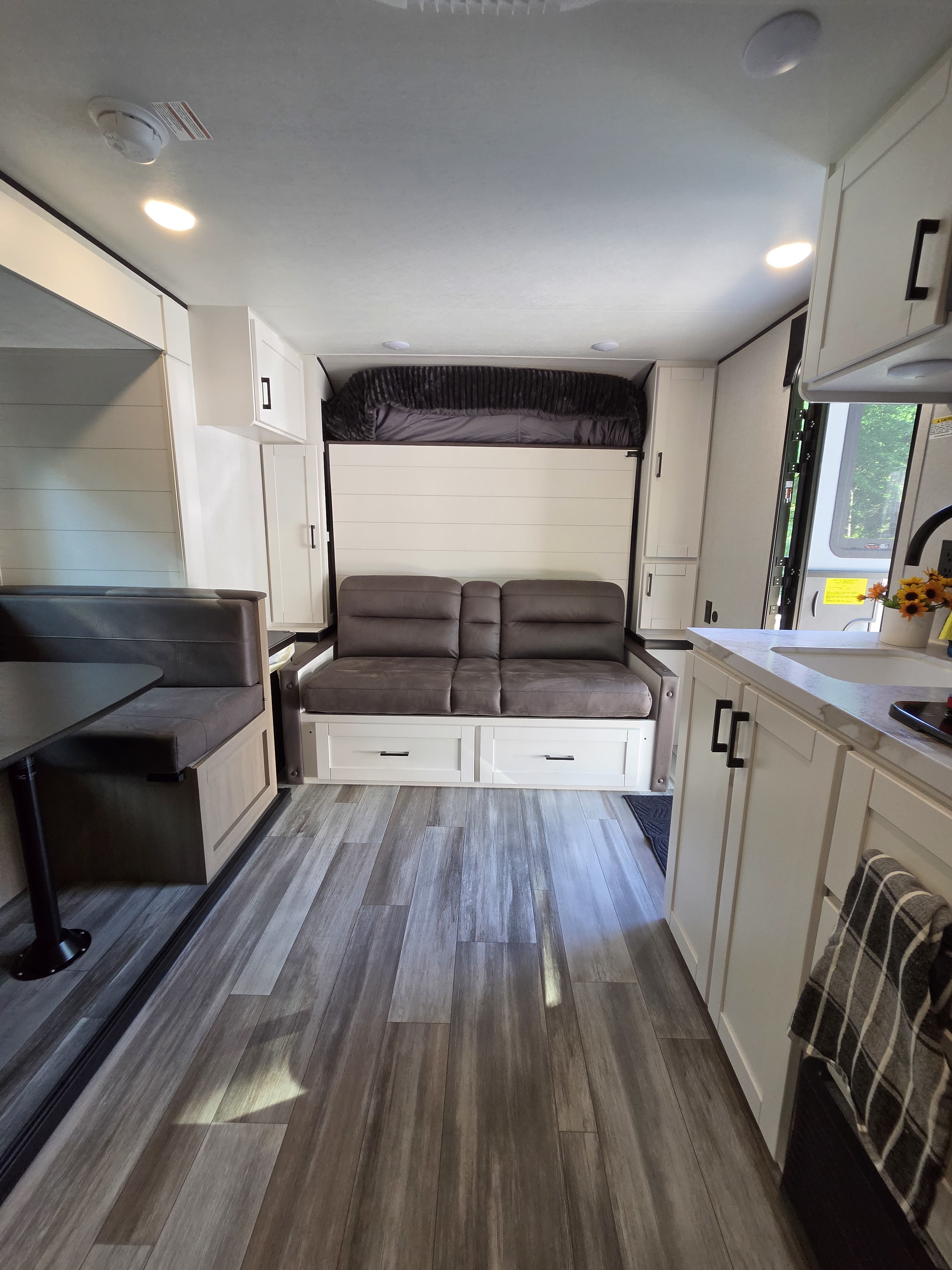 Explore this modern RV rental interior: dinette, sofa, kitchen, and cleverly integrated bunk bed above. Light floors, white cabinets.. Jayco Jay Flight SLX 2026