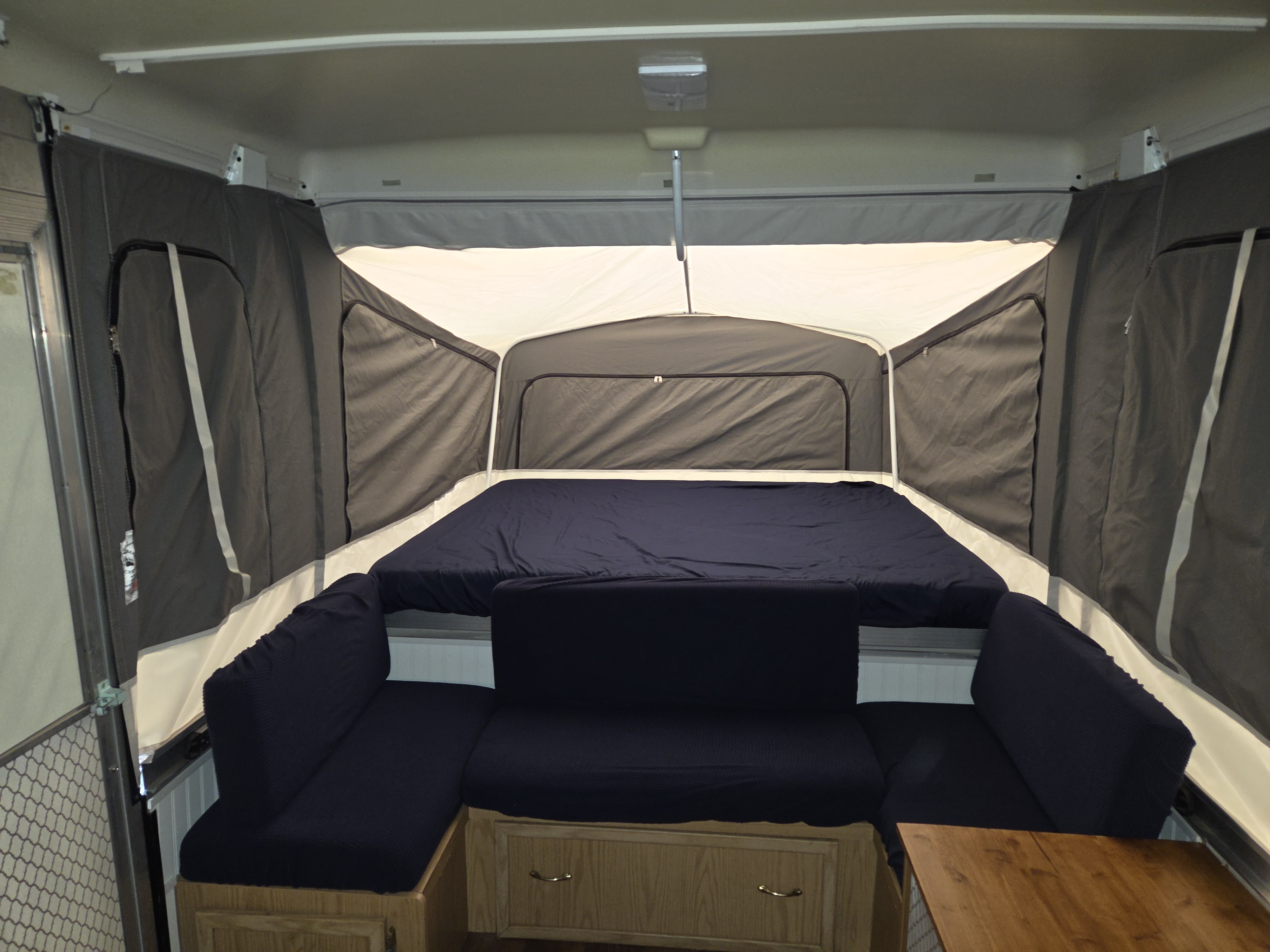 Cozy pop-up camper RV rental interior with a large bed, L-shaped seating, and wooden storage cabinets.. Coleman Grand Tour Mesa 1999