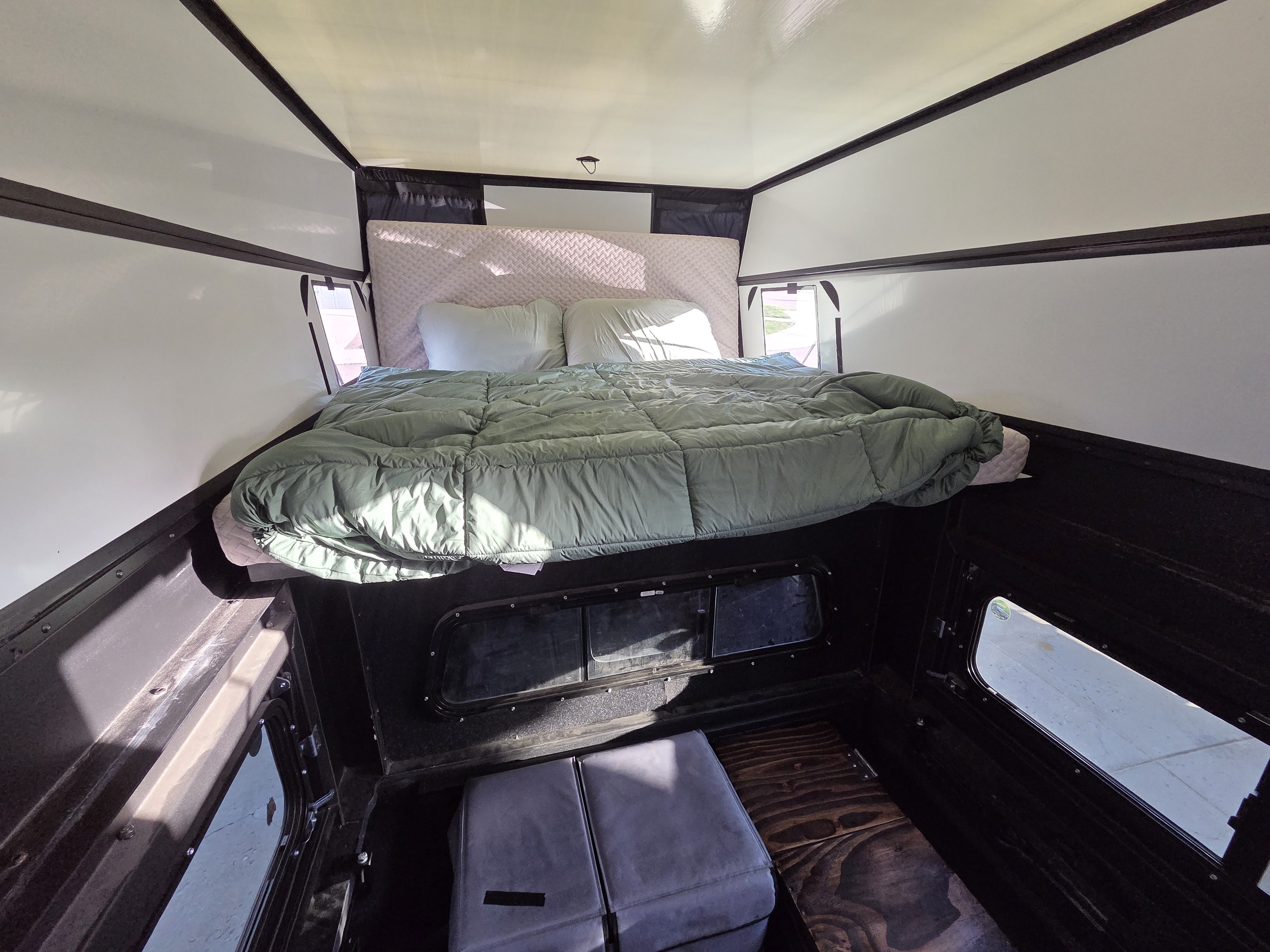 Comfortable RV rental camper interior with an elevated bed, green comforter, pillows, and versatile seating below.. Jeep Gladiator 2020