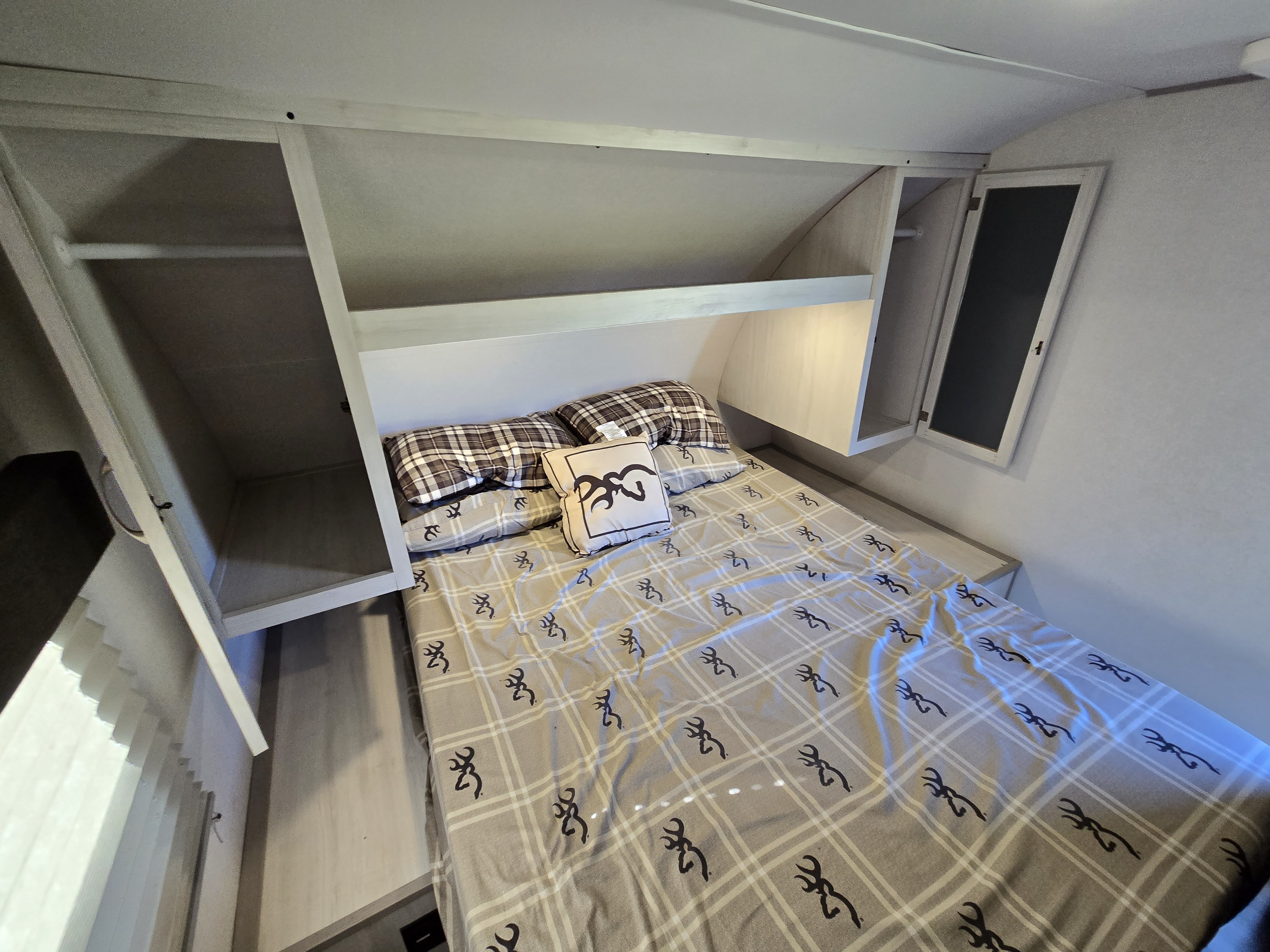 Cozy RV rental bedroom featuring a compact bed with plaid bedding, built-in shelves, and overhead cabinets for storage.. Forest River Tracer 2022