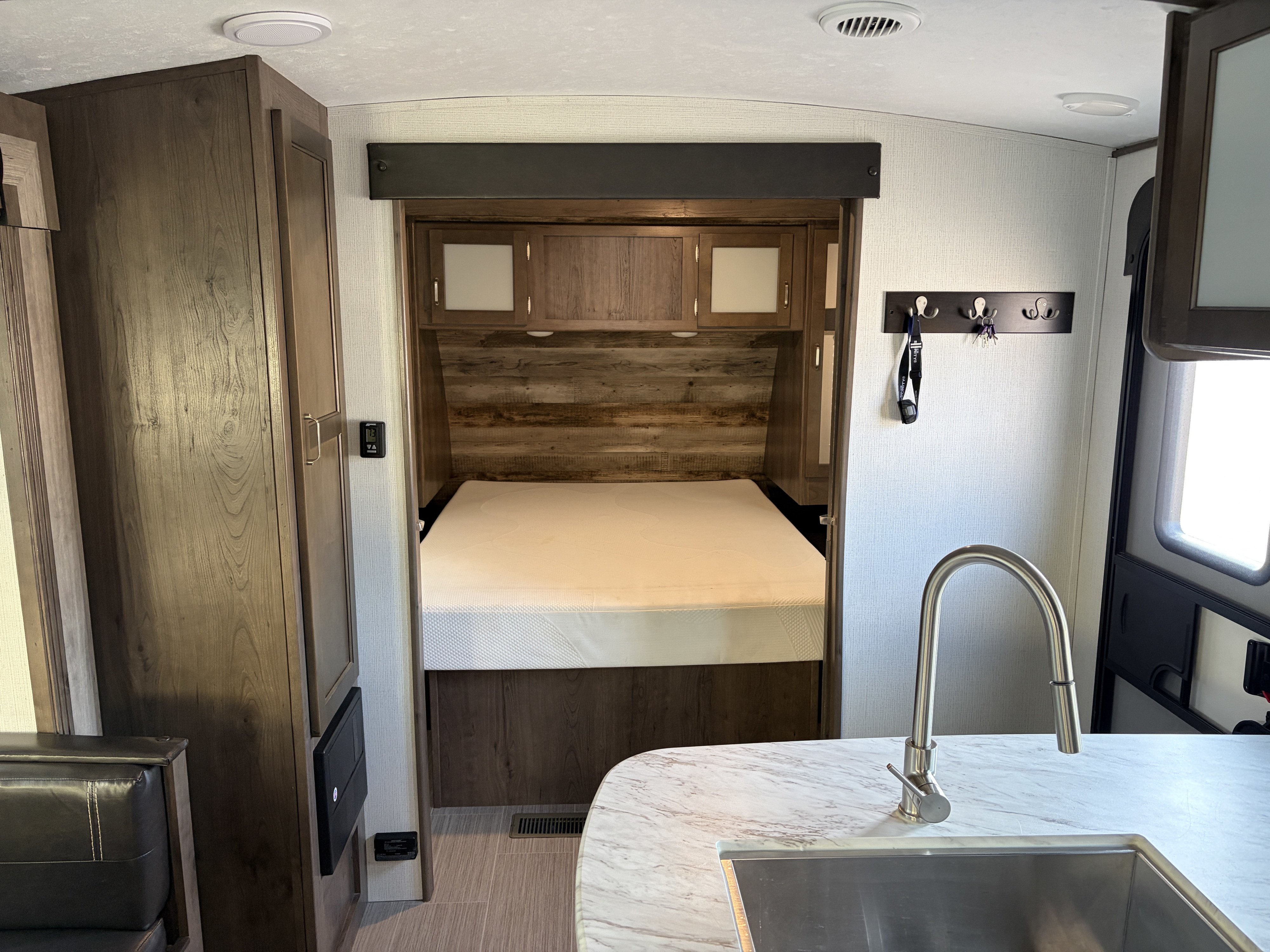Inside an RV rental, showing the clean bedroom with a bed and overhead cabinets, alongside a modern kitchen sink.. Keystone RV Passport GT 2021