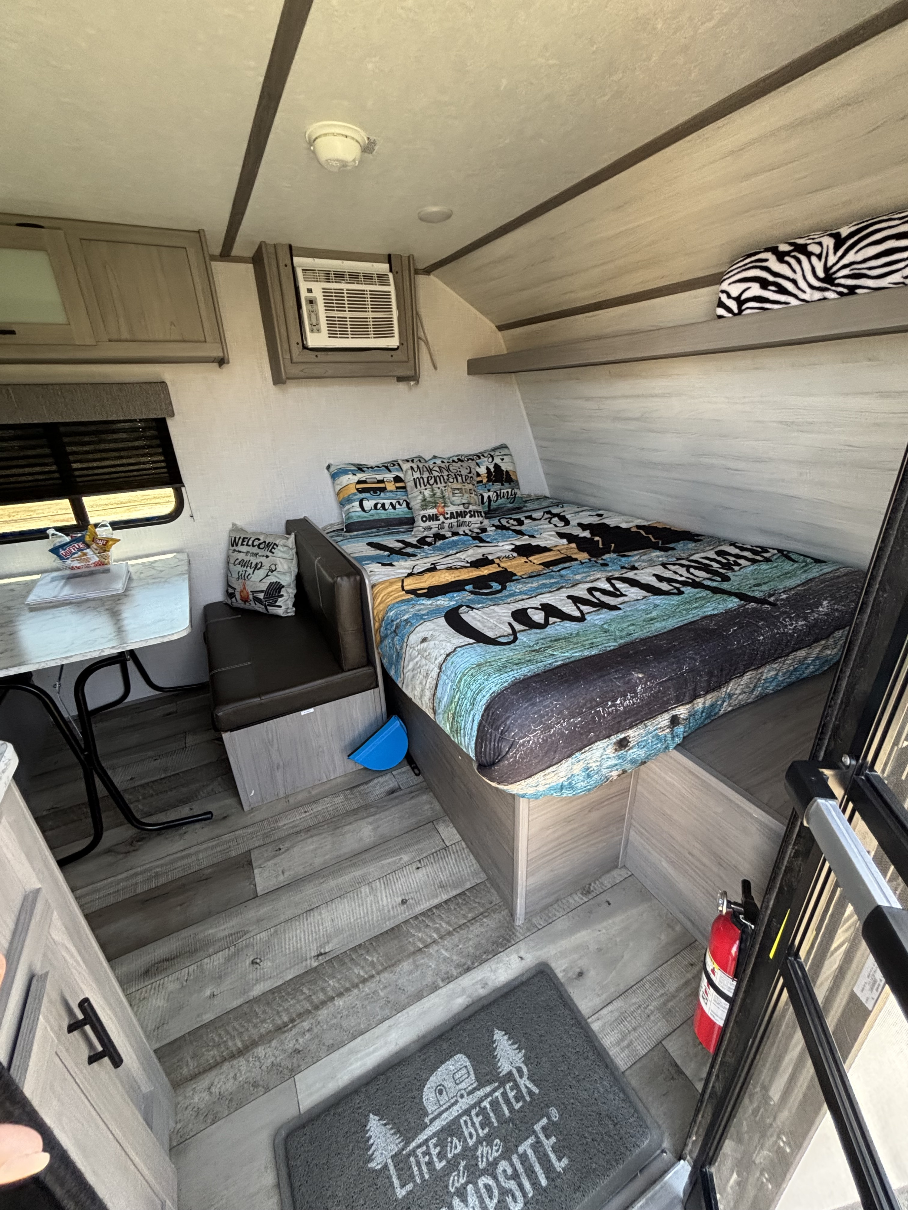 This RV rental interior features a cozy bed with camping linens, a dinette, AC unit, and a fire extinguisher for safe travels.. Dutchmen Coleman Lantern LT 2023