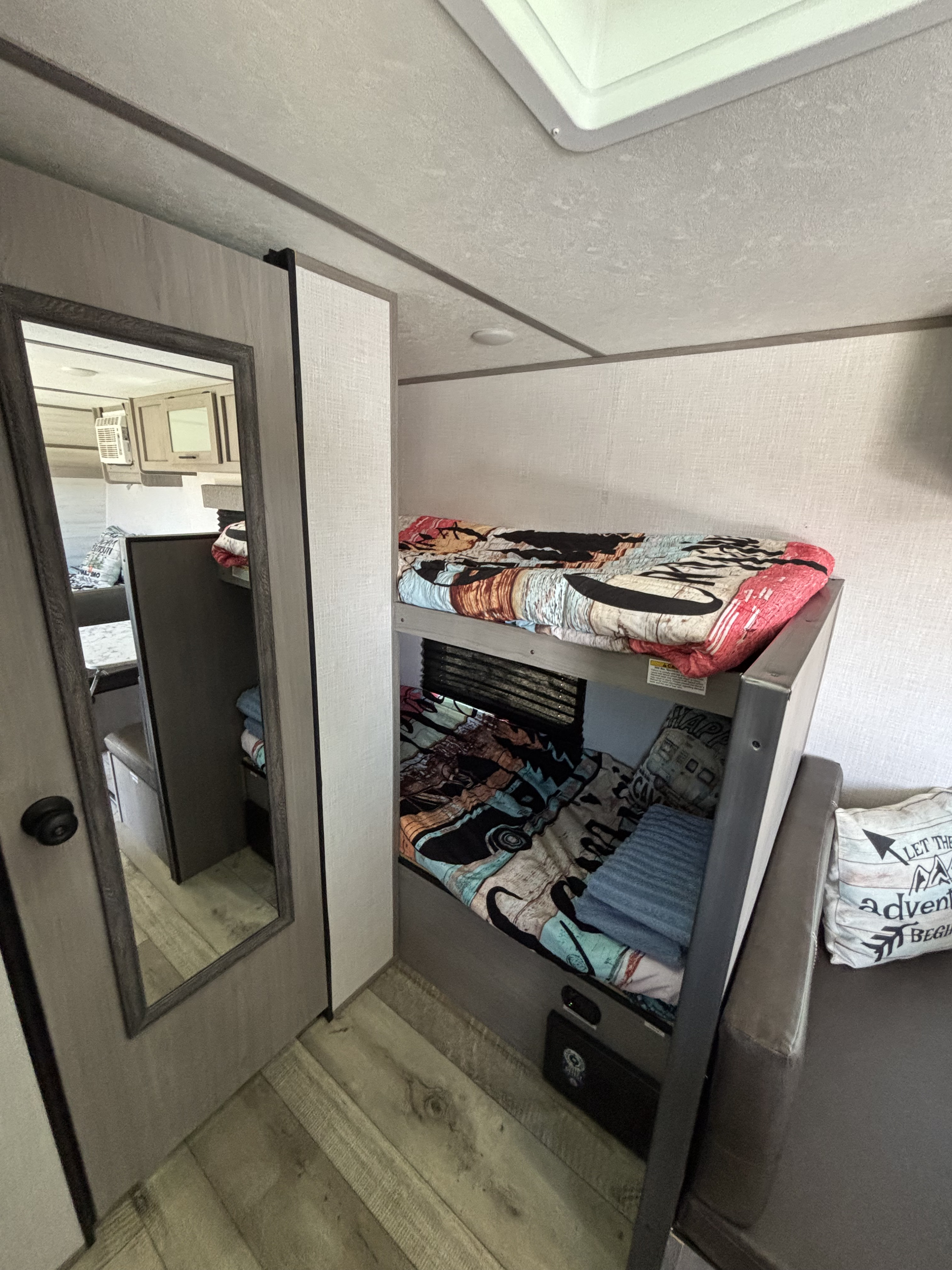 This RV rental interior showcases cozy bunk beds with colorful bedding and a compact living area, ideal for family travel.. Dutchmen Coleman Lantern LT 2023