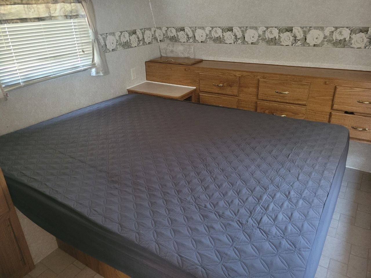 Spacious RV rental bedroom featuring a bed with gray quilted cover, window blinds, and wooden storage cabinets.. Fleetwood 23T6 2004