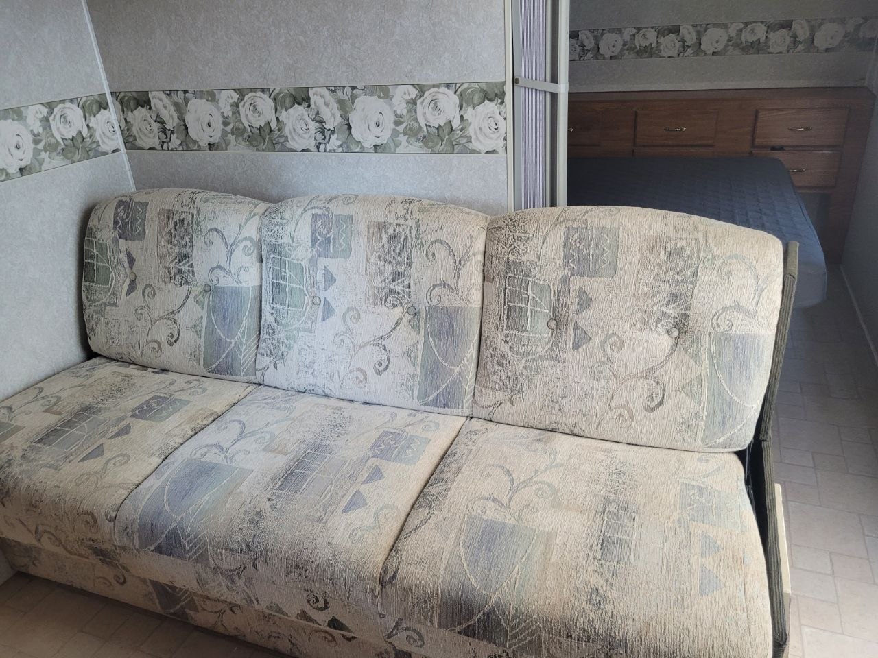 Cozy RV rental interior with patterned sofa and glimpse into the bedroom, featuring wood cabinetry and a bed.. Fleetwood 23T6 2004