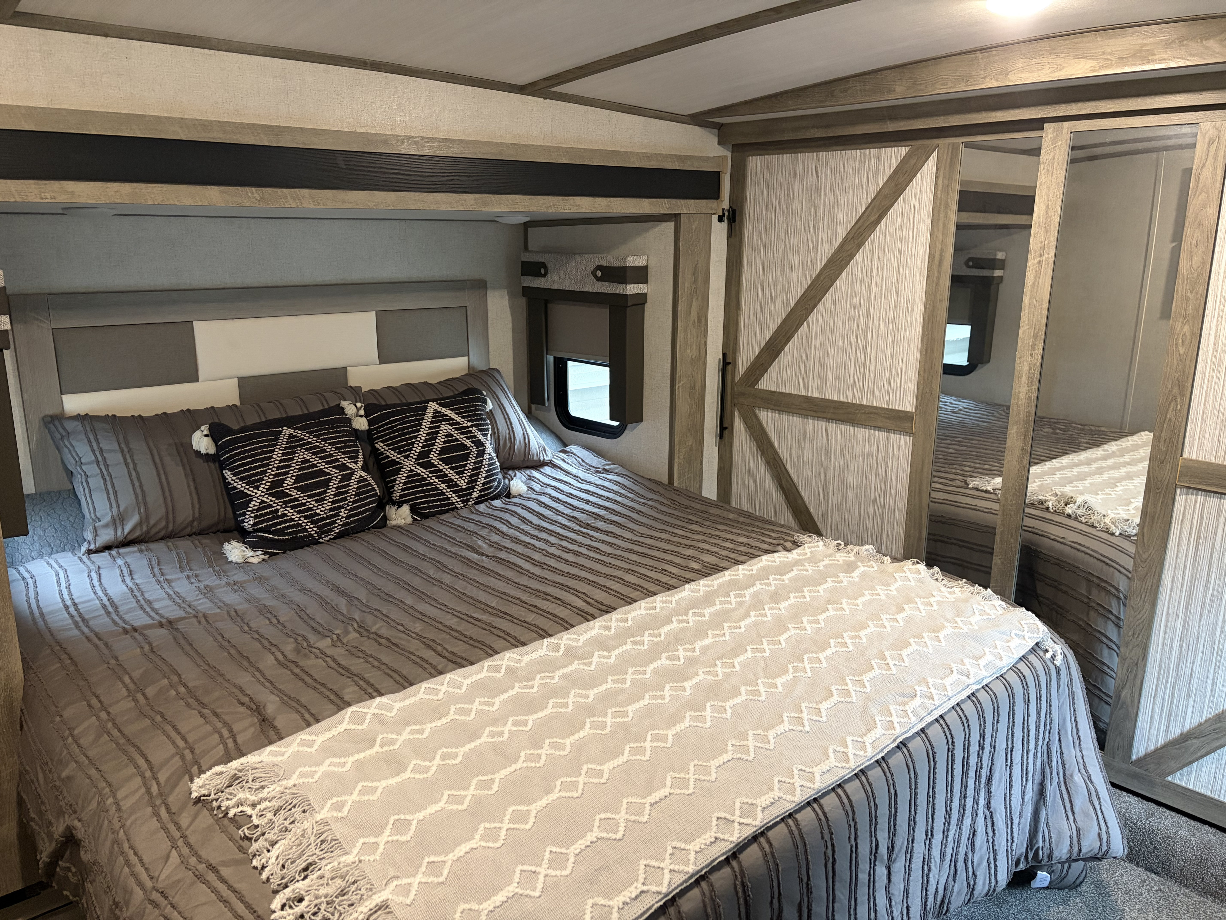 Cozy RV rental bedroom featuring a modern bed with grey bedding, decorative pillows, and a sliding mirrored closet.. Forest River Salem Hemisphere 2021